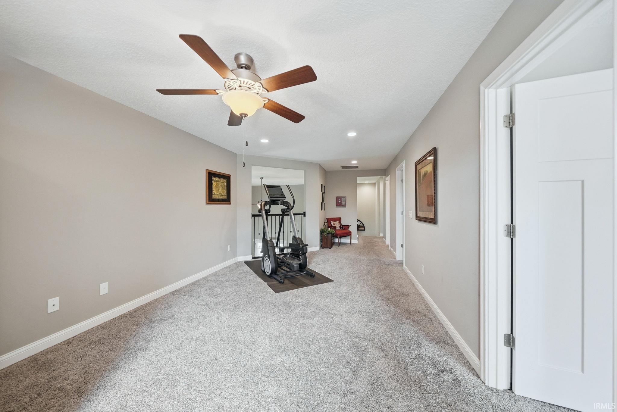 Spacious carpeted hallway featuring a ceiling fan with integrated lighting, recessed lighting, and light gray wall finishes