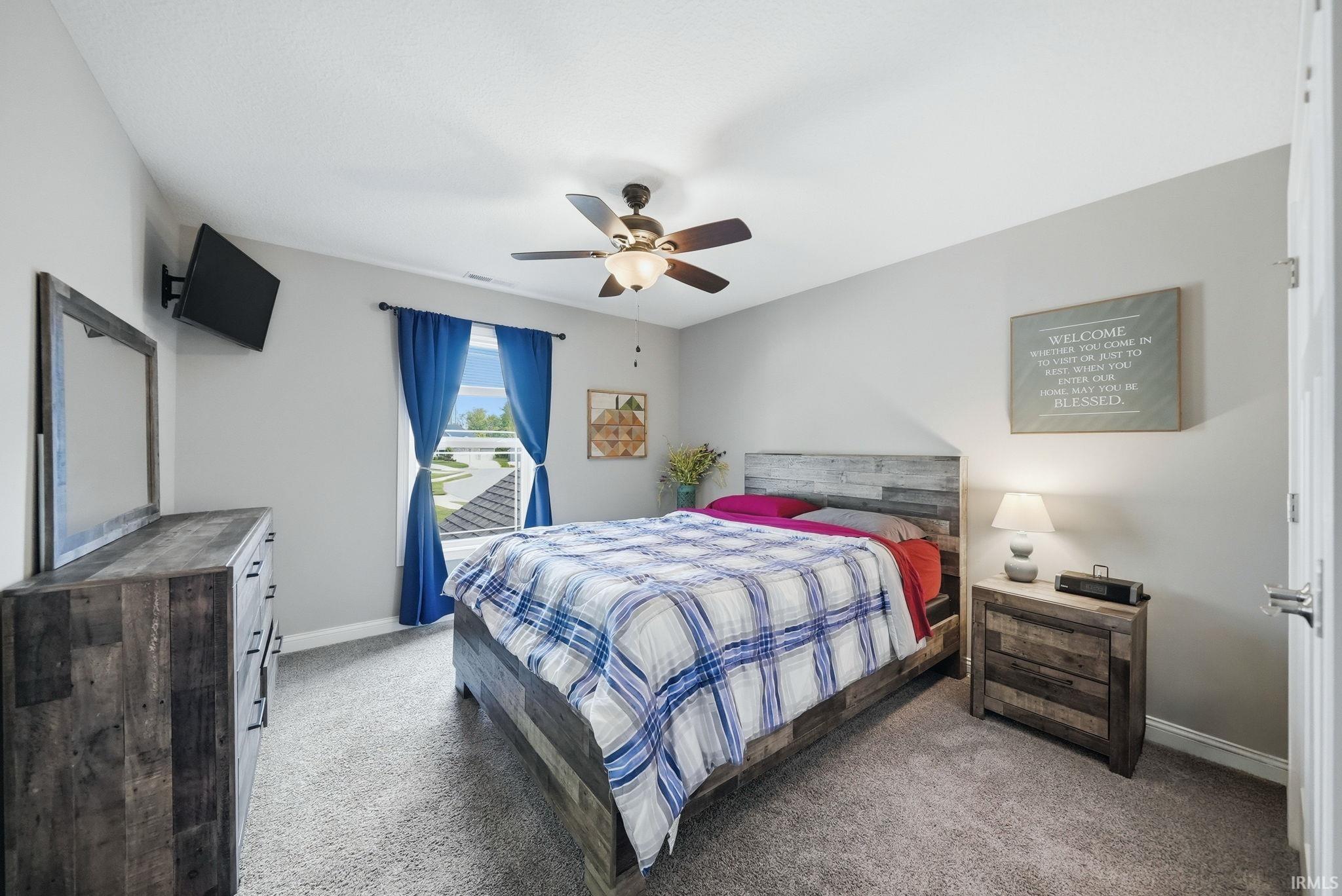 Carpeted bedroom with a window offering natural light, a ceiling fan with integrated lighting, and light grey wall finishes