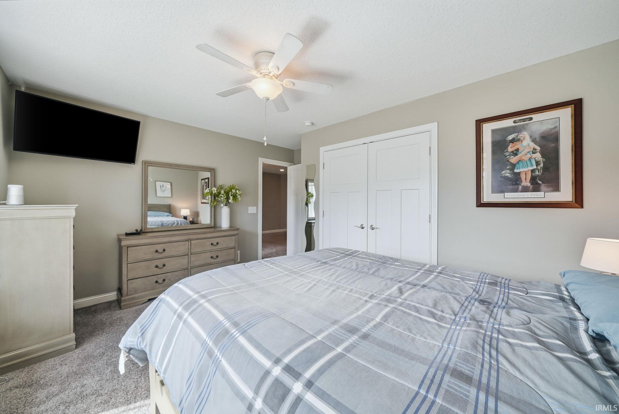 Carpeted bedroom featuring a ceiling fan with integrated lighting, neutral wall tones, and white bi-fold closet doors