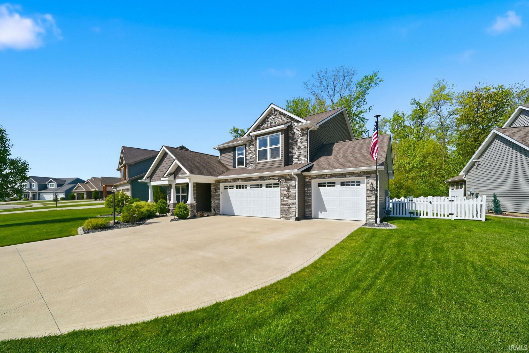 Two-story residence featuring stone and siding facade, an expansive concrete driveway, and a two-car garage