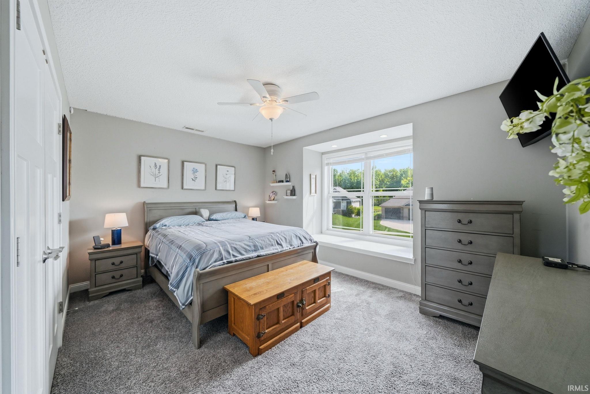 Spacious bedroom featuring a large window with a deep sill, neutral wall color, ceiling fan, and plush carpet flooring