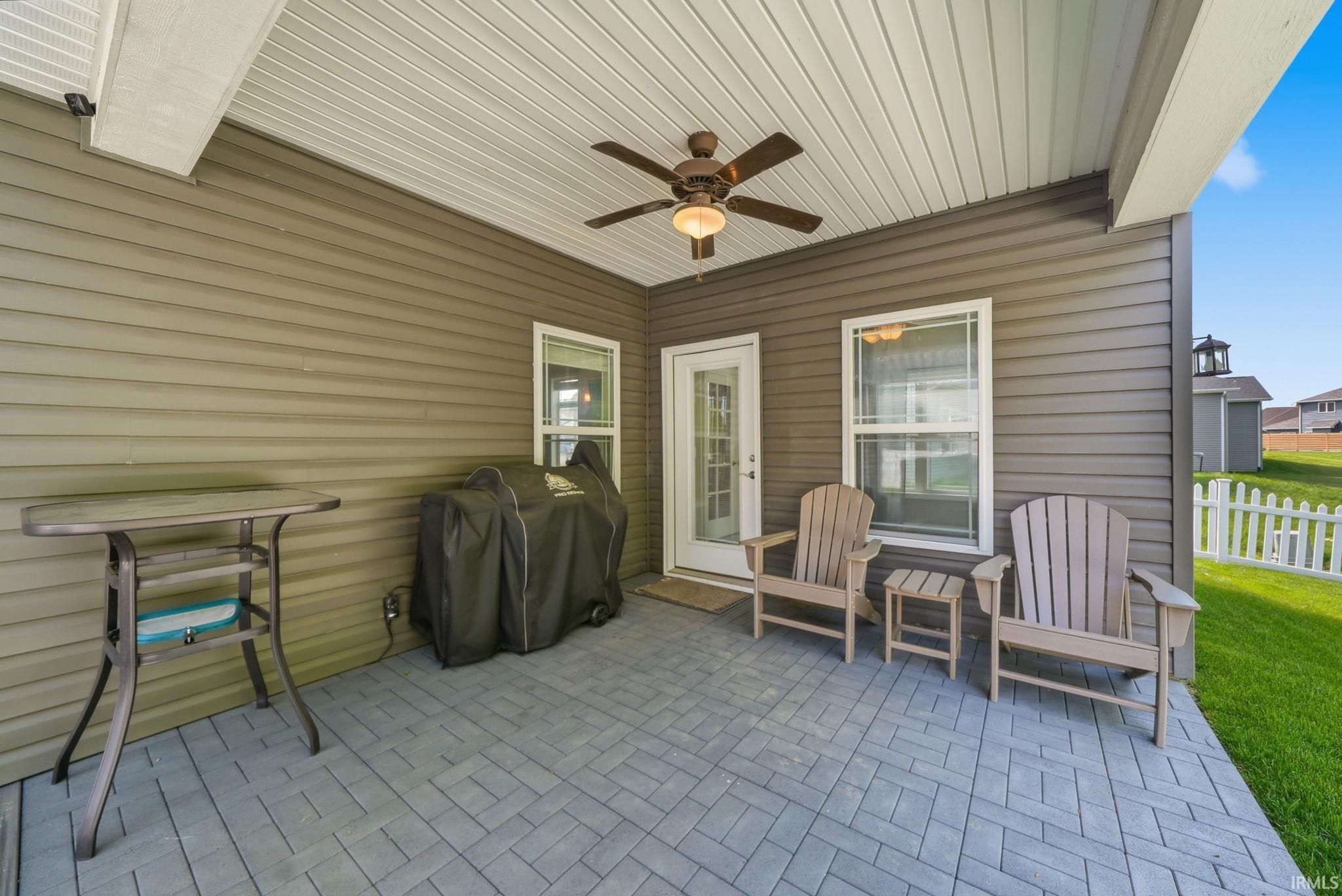 Covered patio with a patterned paver floor, ceiling fan, and white picket fencing