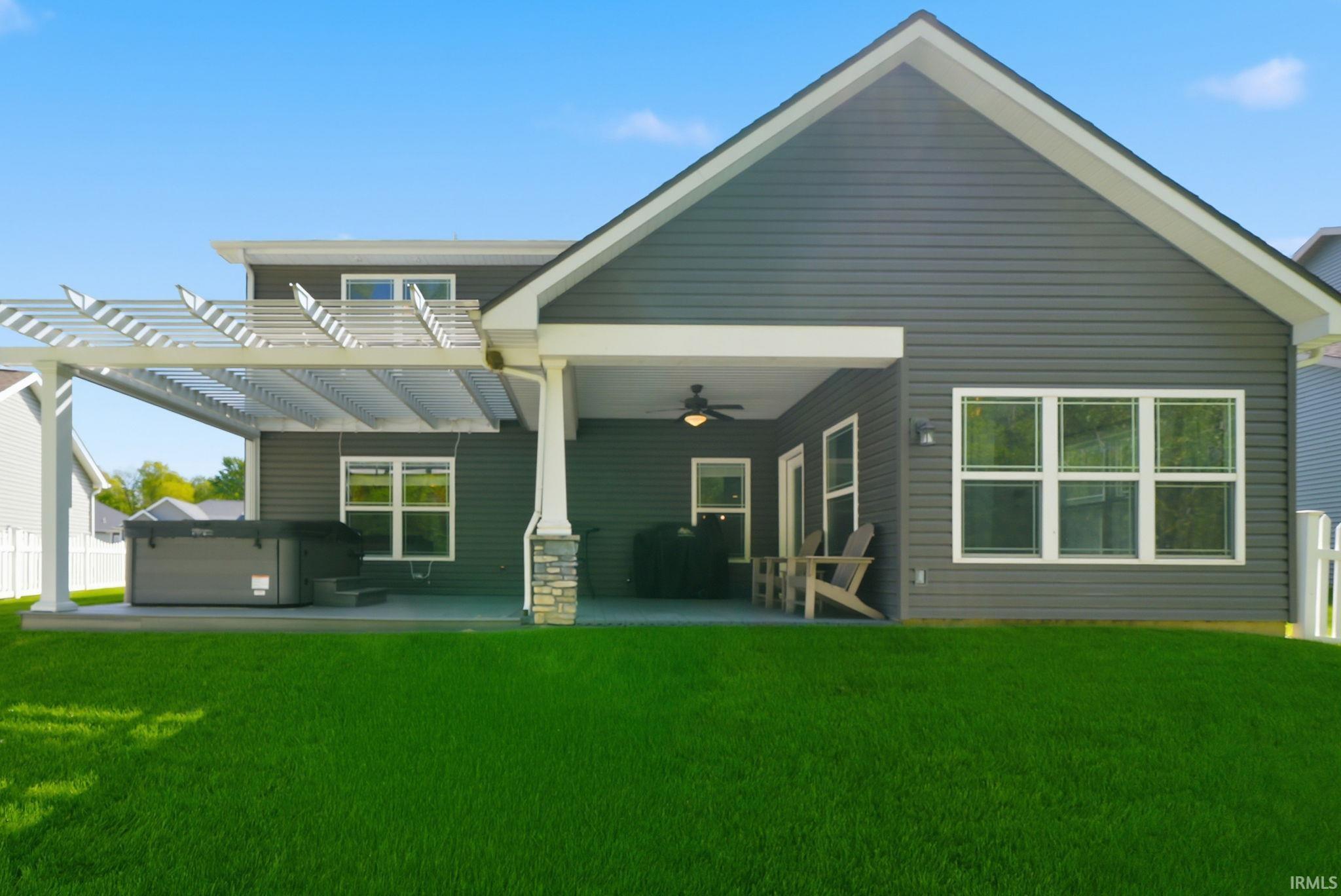 Expansive backyard featuring a manicured lawn, covered patio with a ceiling fan, and an extended pergola