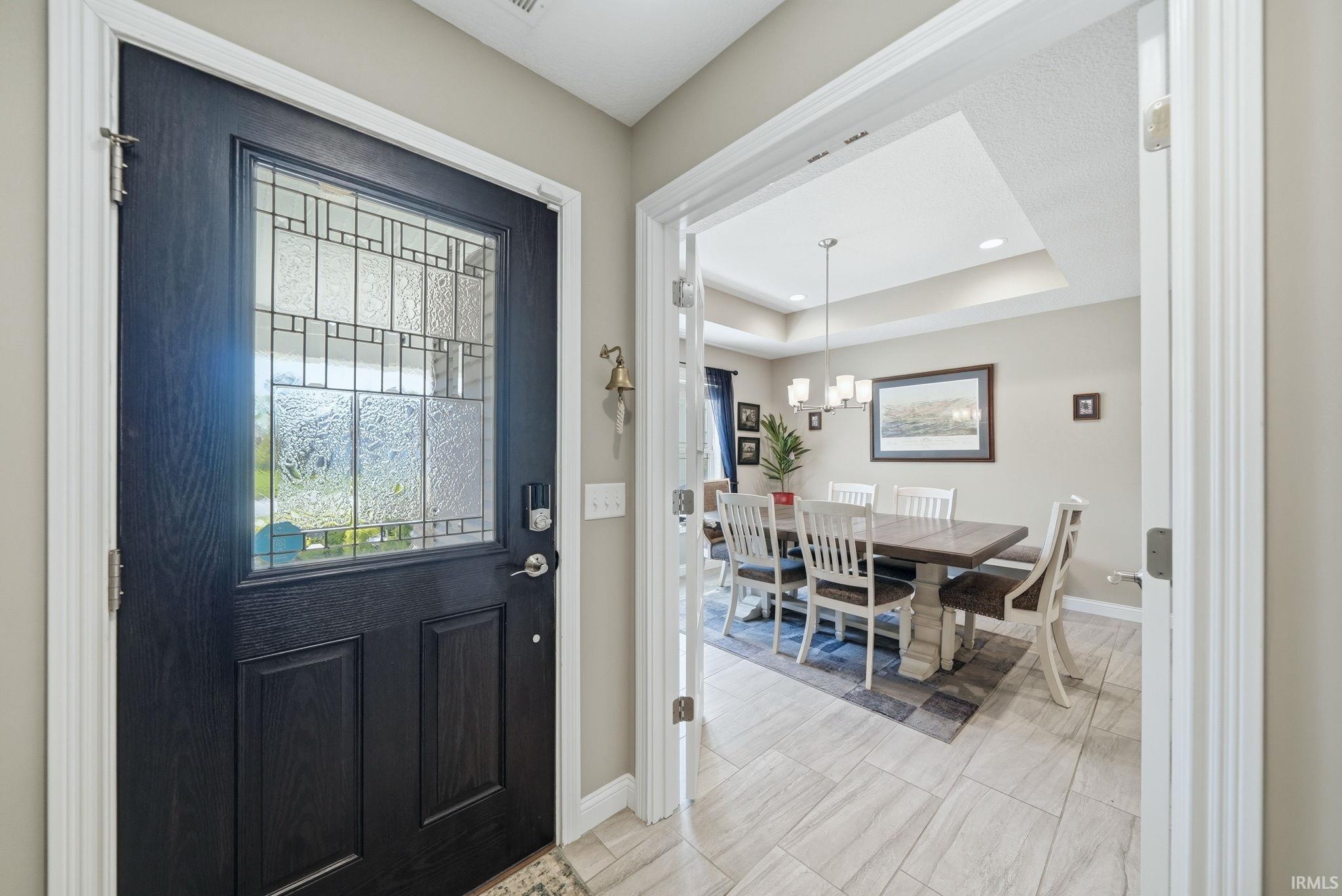 Entryway featuring a dark paneled door with decorative glass, tiled flooring, and a broad cased opening to a formal dining room with a tray ceiling and recessed lighting