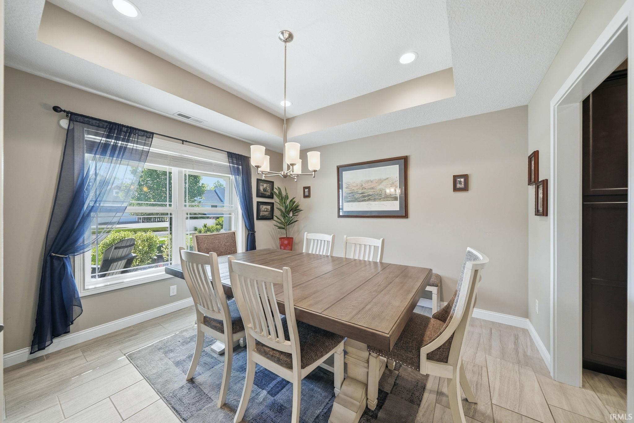 Dining area featuring a tray ceiling, recessed lighting, a modern chandelier, a large window, and light-toned tile flooring