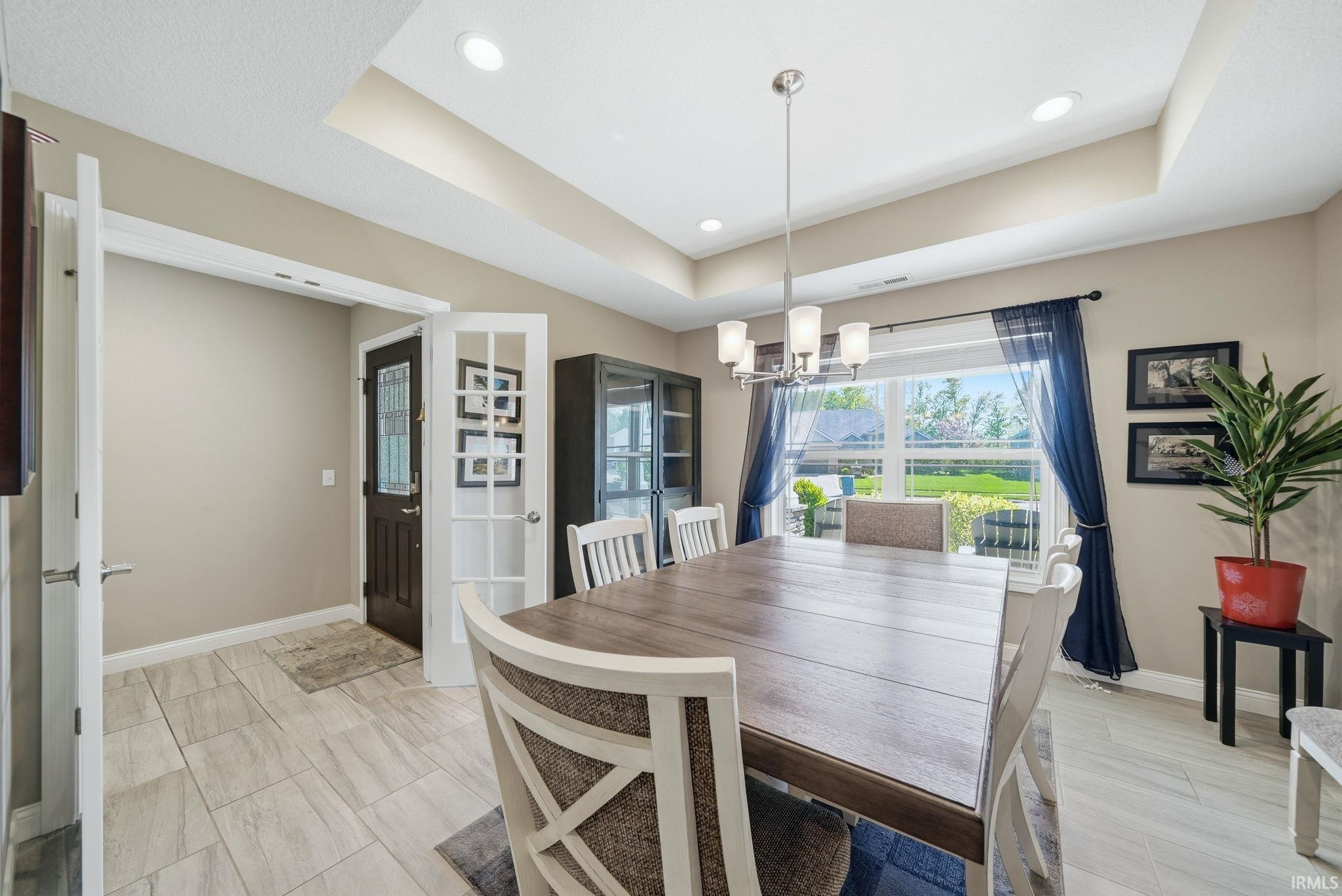 Spacious dining area featuring a tray ceiling, recessed lighting, and a modern chandelier