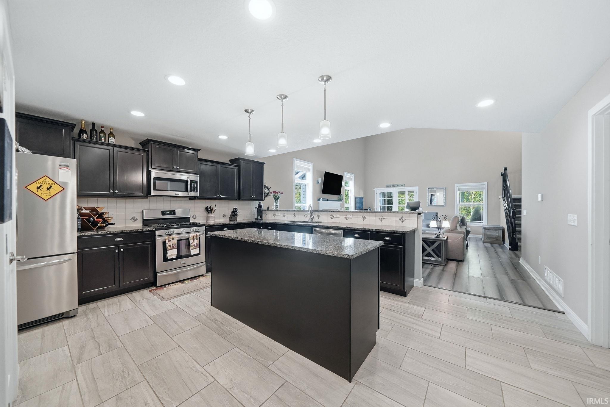 Spacious kitchen featuring dark cabinetry, stainless steel appliances, a center island with a granite-style countertop, and recessed lighting