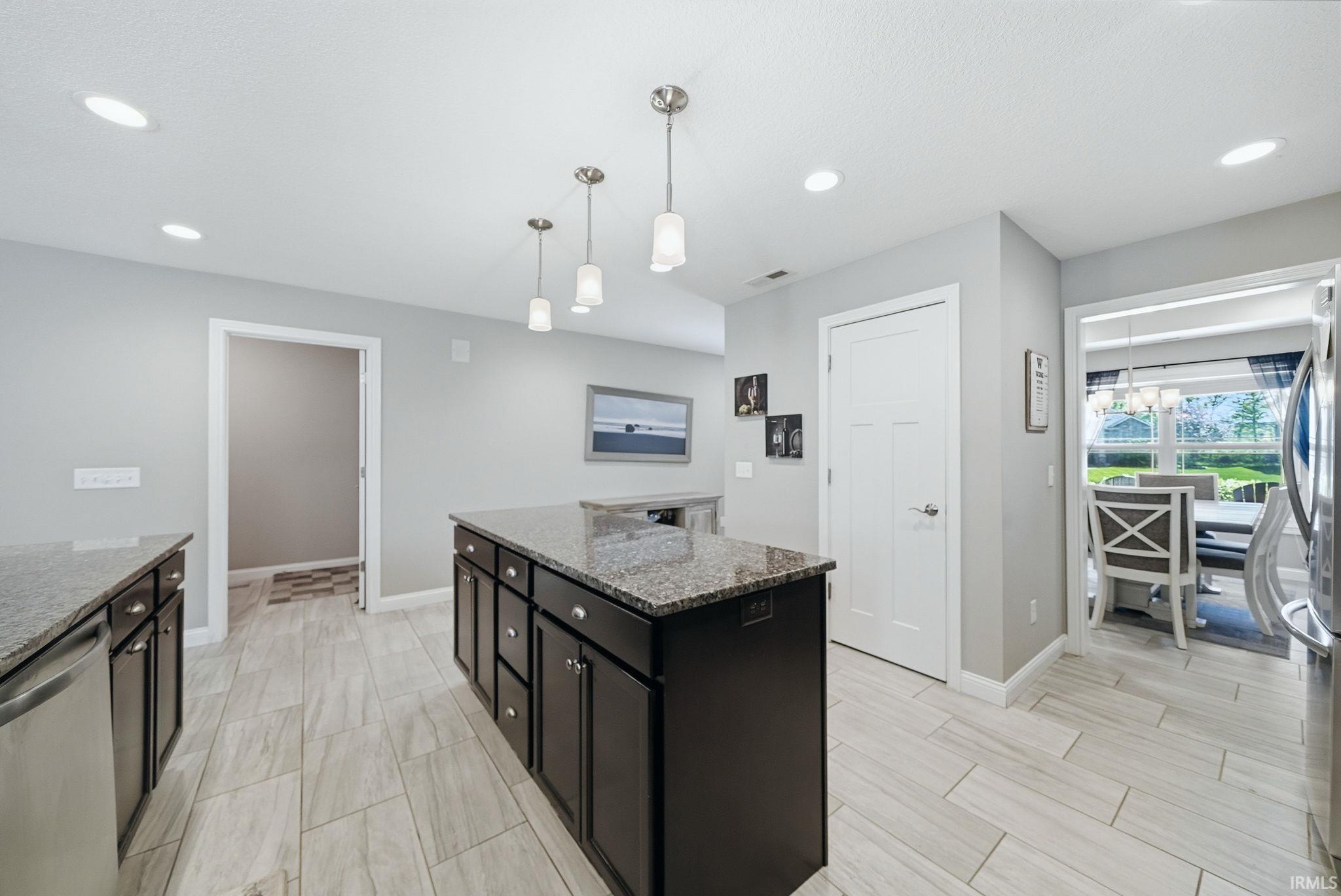 Kitchen featuring a large island with dark cabinetry and speckled countertops, recessed lighting, pendant lighting, and wood-finish tile flooring