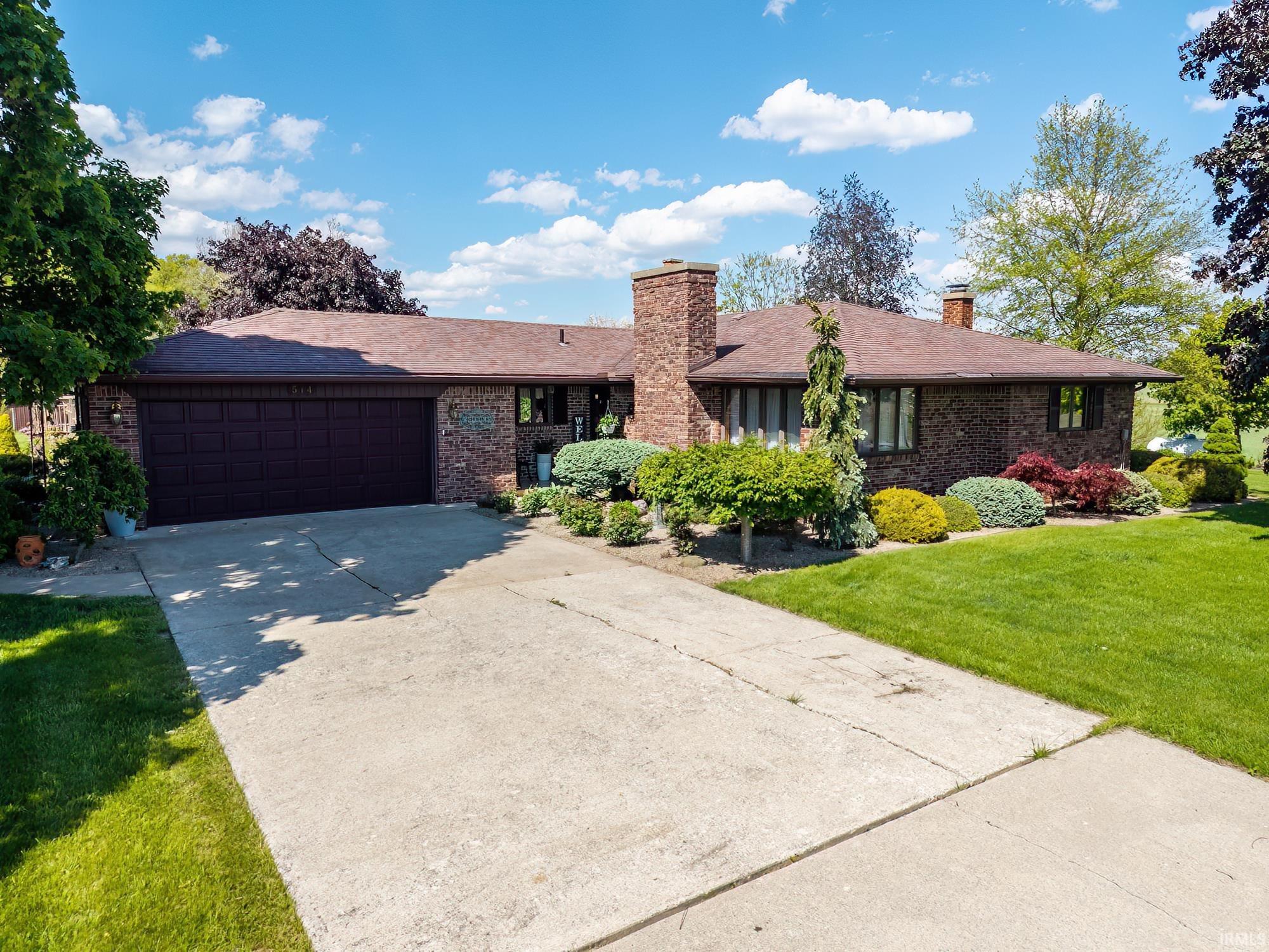 Brick ranch-style residence featuring a two-car garage, concrete driveway, and established front landscaping