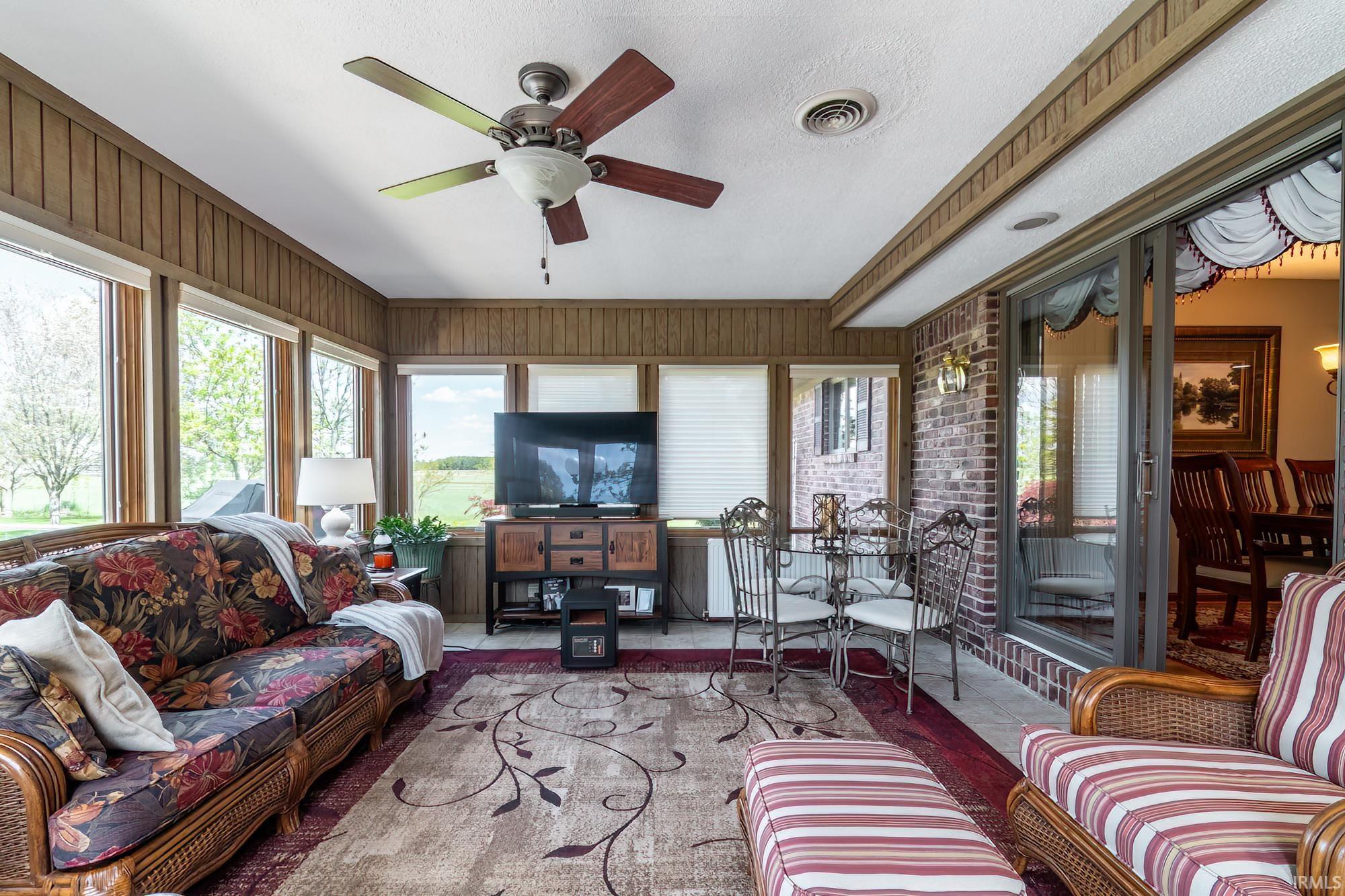 Sunroom featuring extensive window-lines, wood-panel wall finishes, a ceiling fan, and a brick accent wall with sliding glass door access
