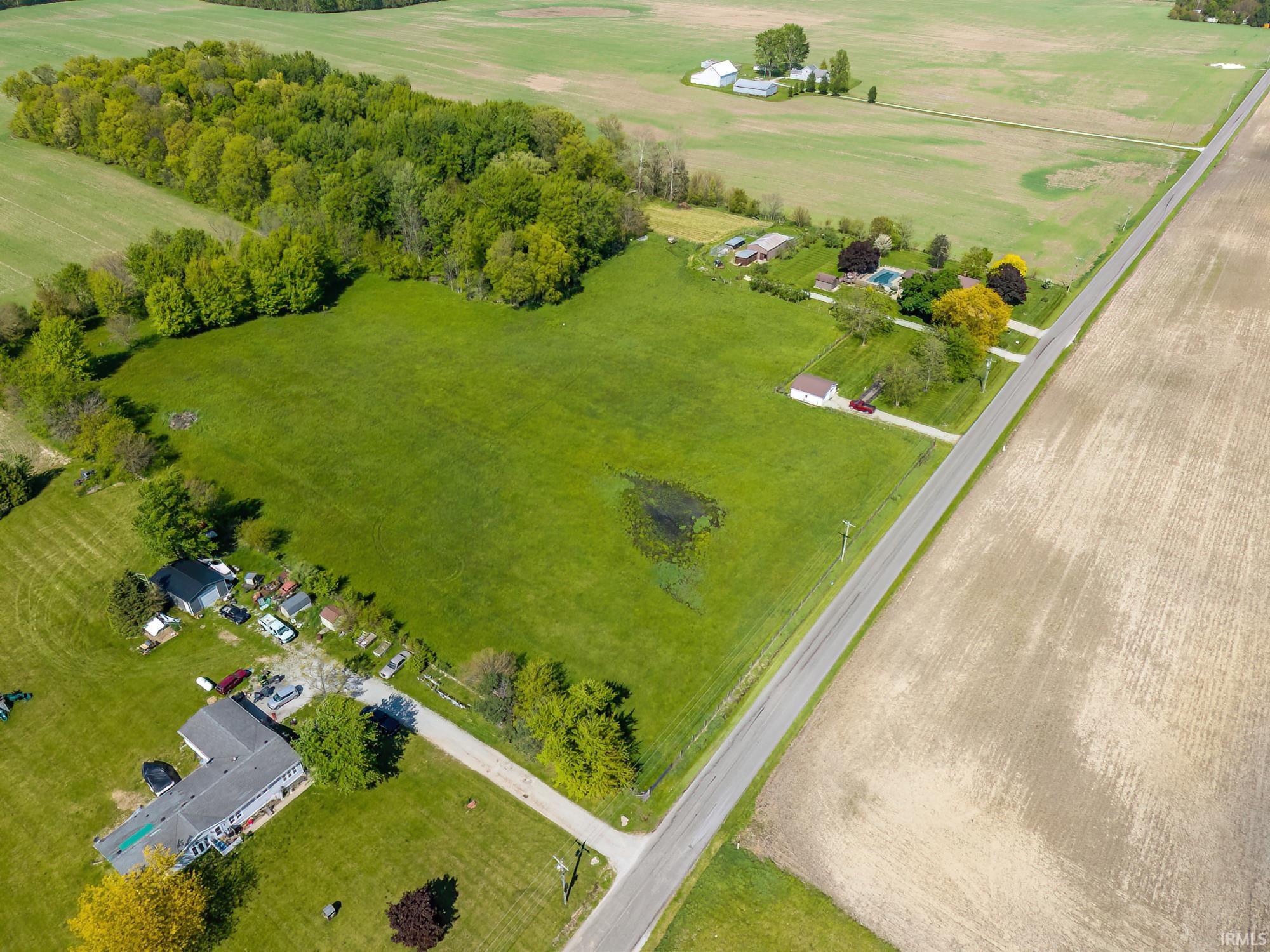 Expansive rural property featuring substantial green acreage, mature tree lines, and multiple structures