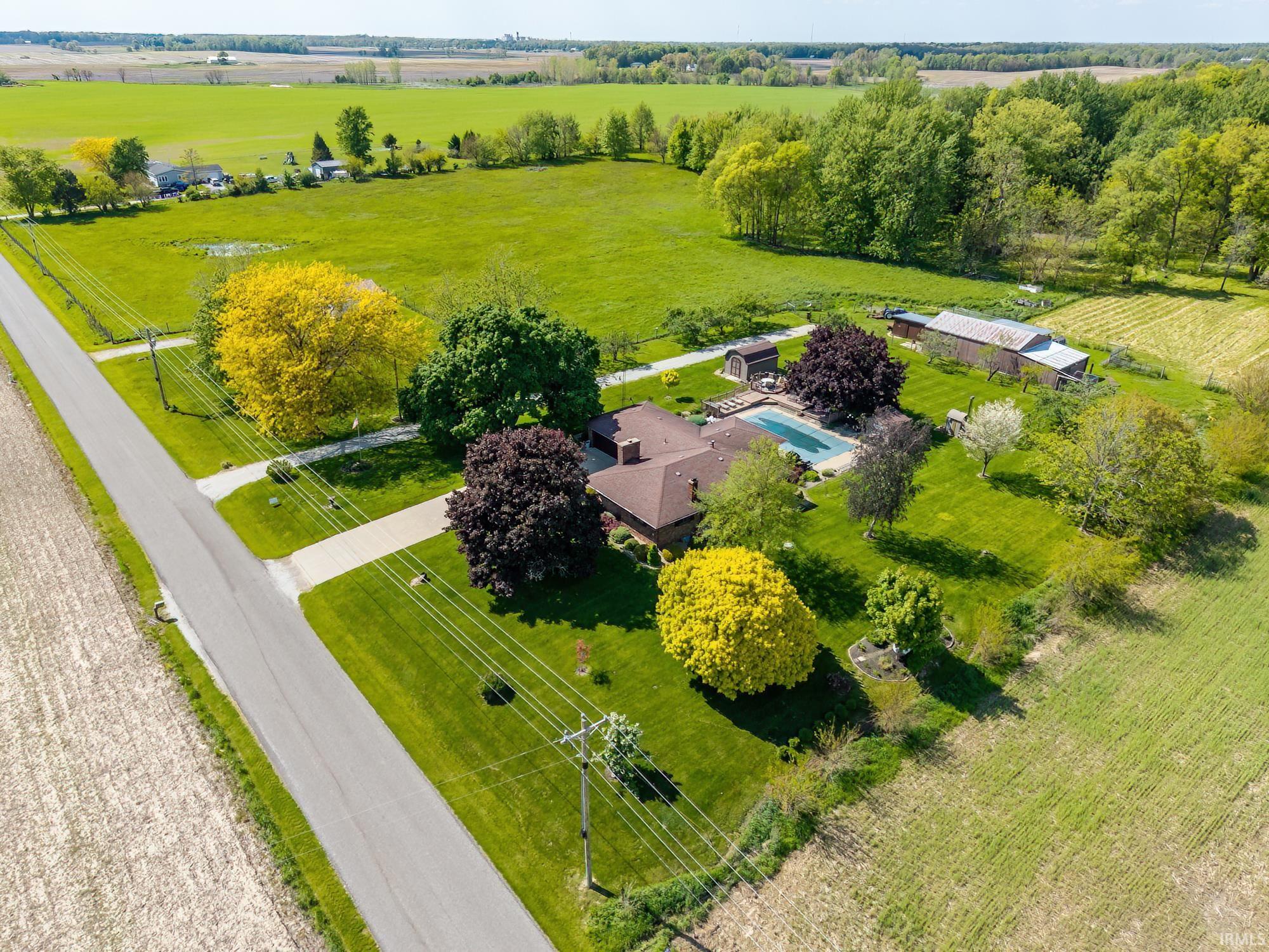 Expansive property featuring a brown-roofed residence, a rectangular in-ground pool, and a gravel driveway