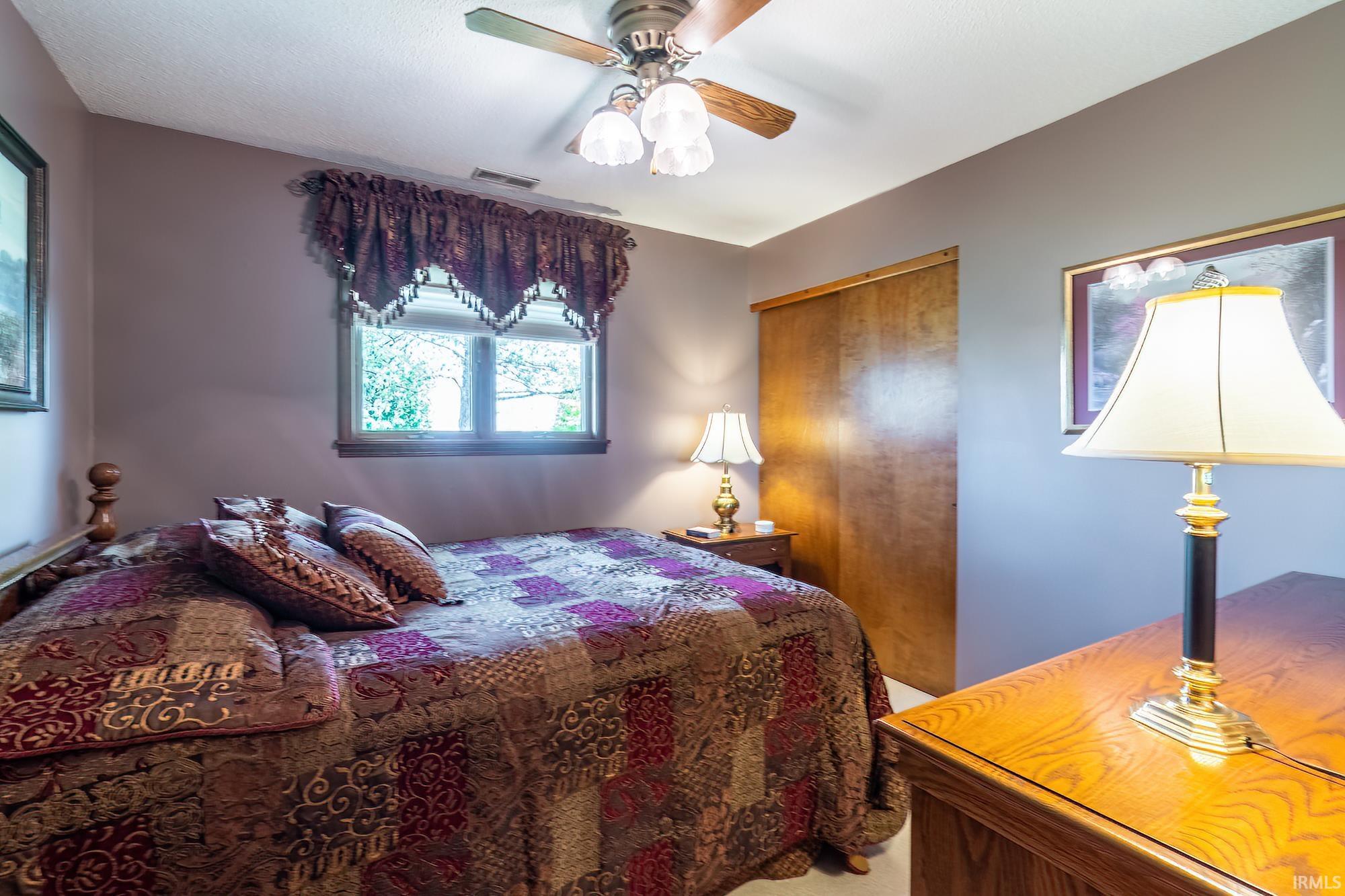 Bedroom featuring a ceiling fan with integrated lighting, wood-finish sliding closet doors, and light-colored carpeting