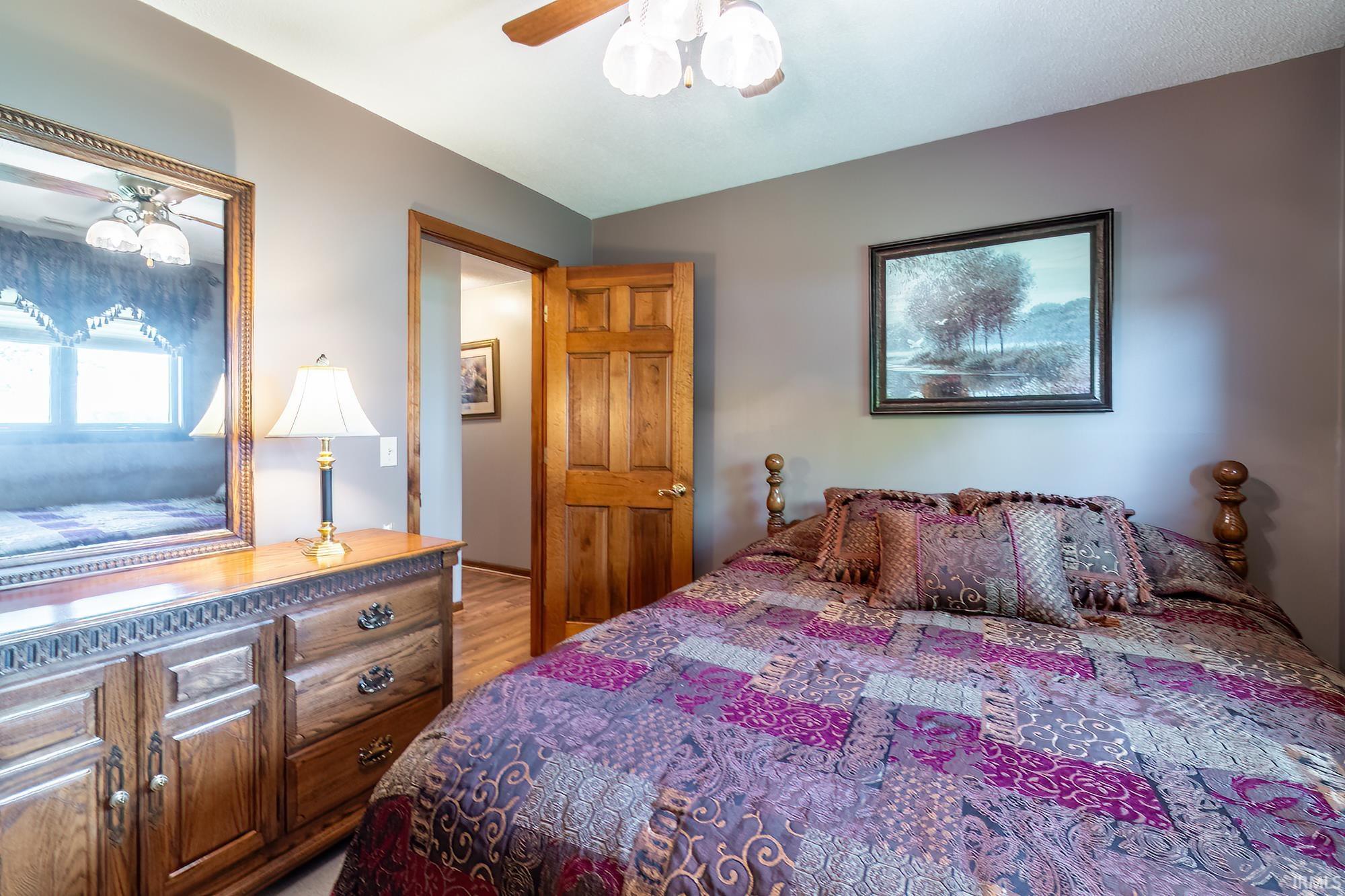 Bedroom featuring warm gray walls, wood-finish flooring, a paneled wood door, and a ceiling fan with light fixture