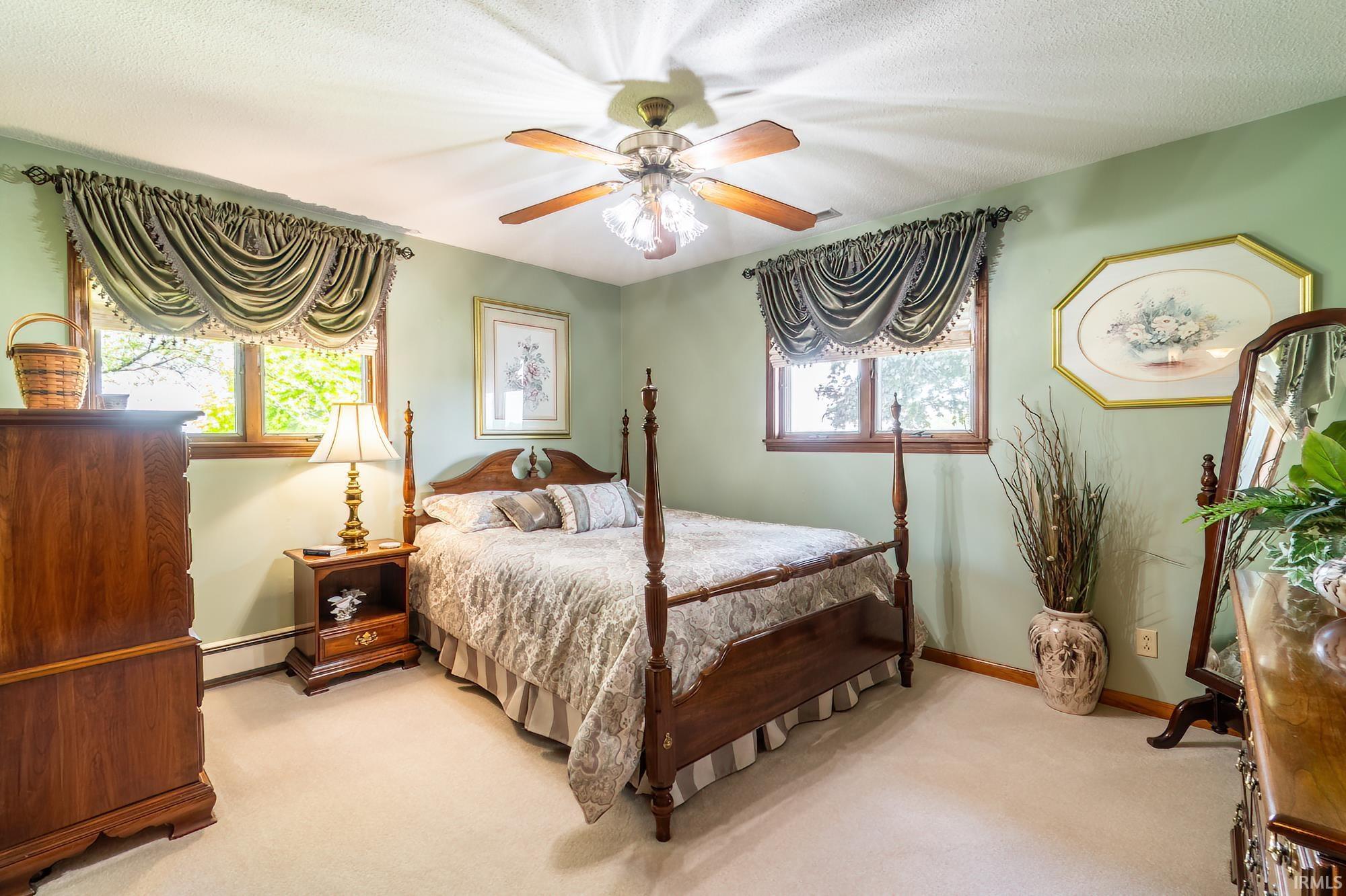 Bedroom featuring two windows with decorative valances, a ceiling fan with integrated lighting, wood-trim windows, and light-colored carpeting