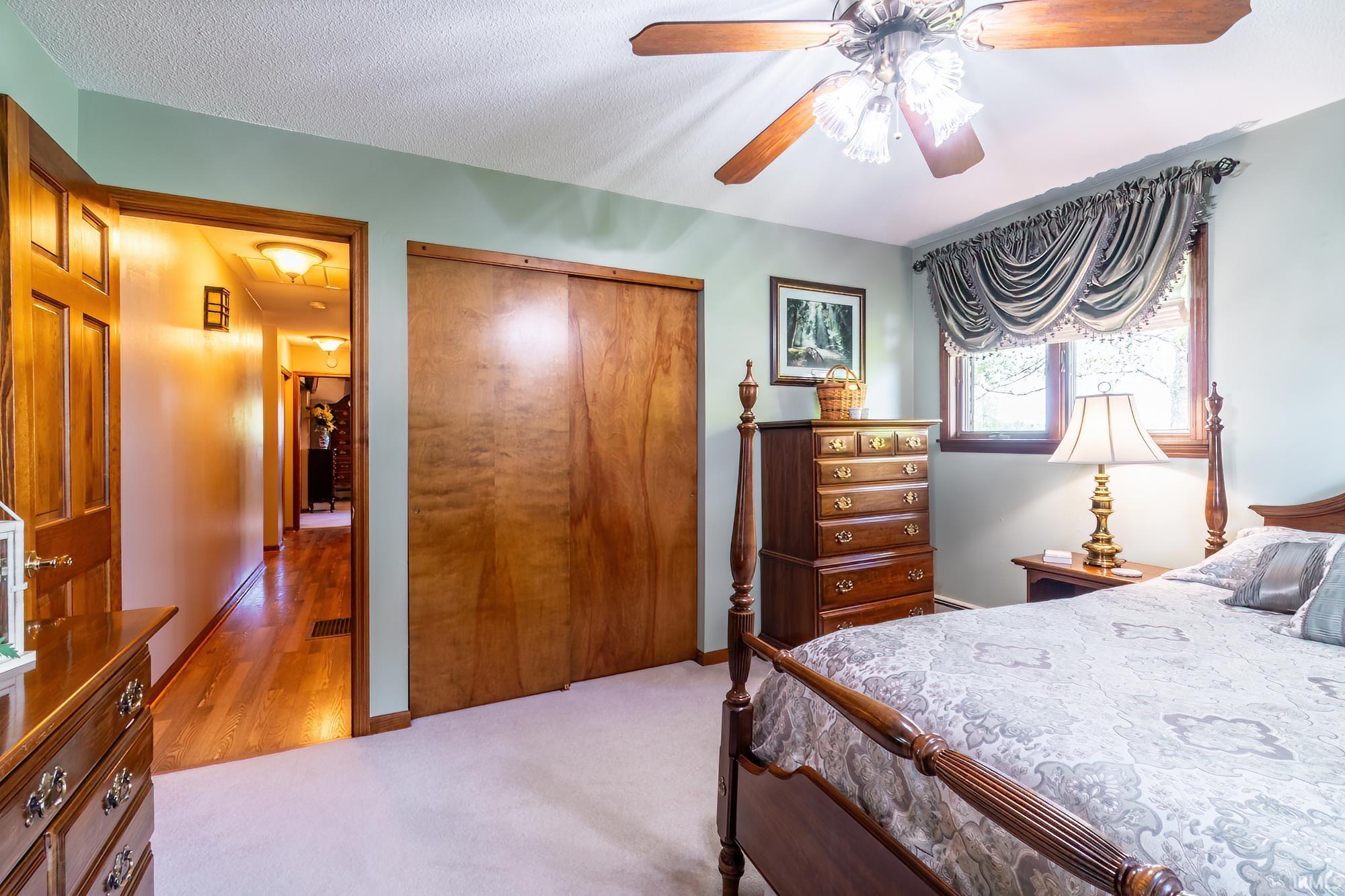 Spacious room featuring light green walls, light-toned carpeting, and a wood-finish ceiling fan with integrated lighting