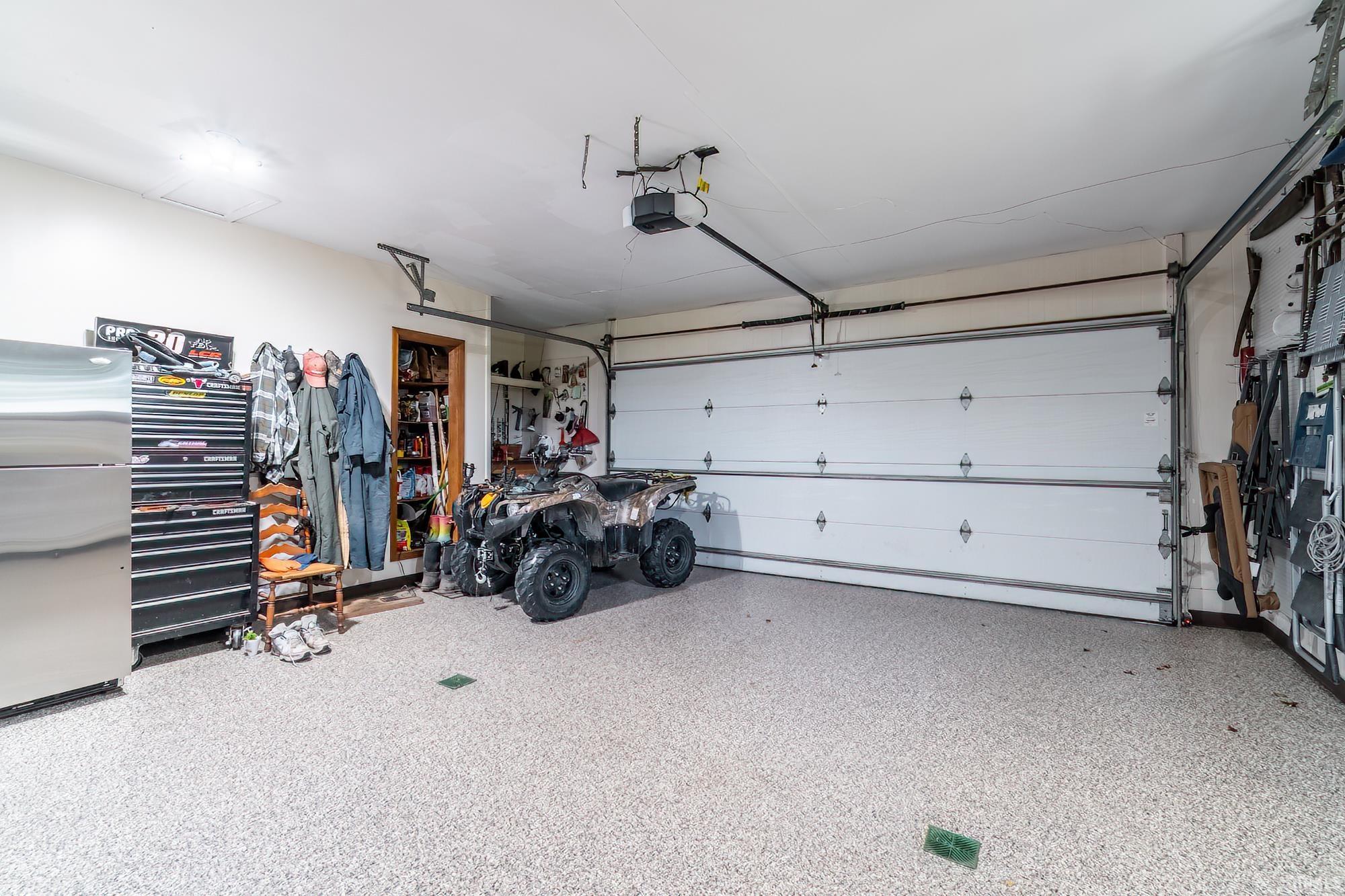 Spacious garage featuring a speckled epoxy floor, white paneled garage door, exposed ceiling joists, and built-in shelving