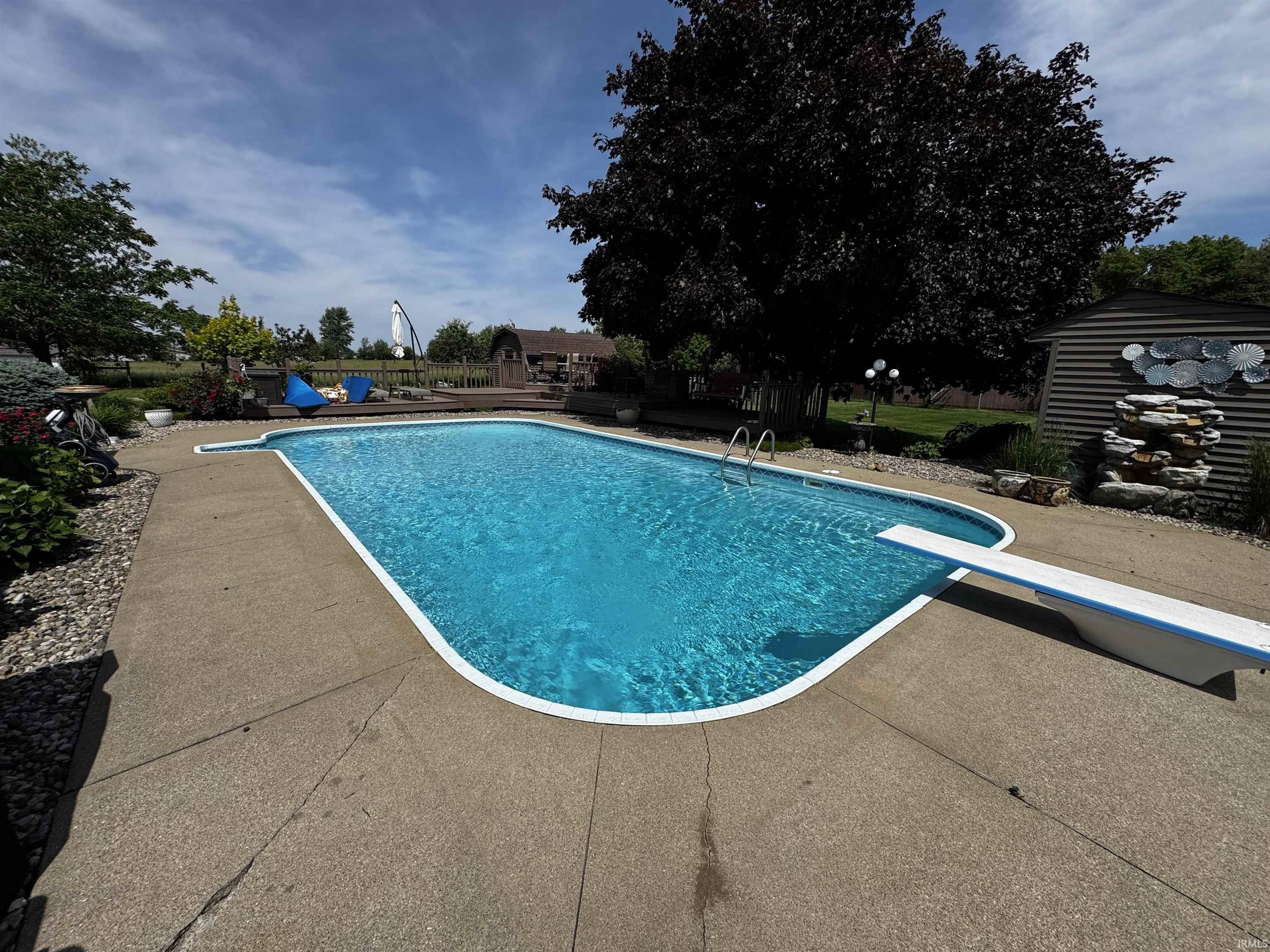 Rectangular inground pool with a diving board, surrounded by an exposed aggregate concrete patio