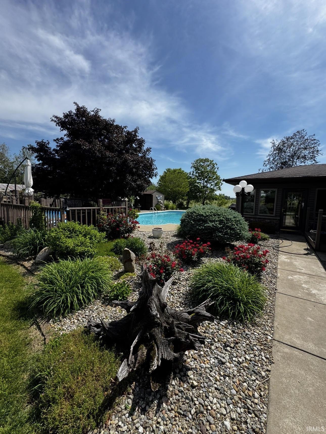 Outdoor swimming pool surrounded by a gravel landscape bed with various plantings, including green shrubs and red flowering bushes