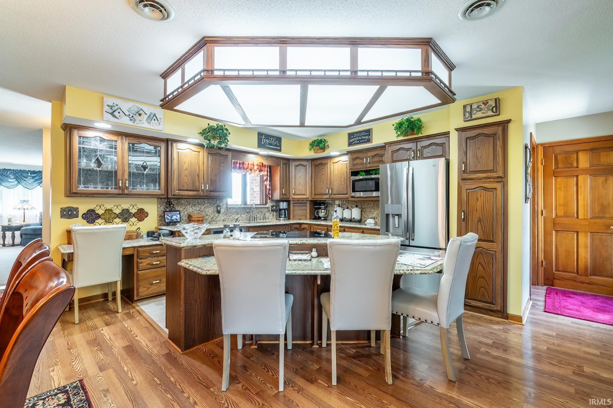 Open-concept kitchen with wood-finish flooring, recessed lighting, wood cabinetry, granite-style countertops, and stainless steel appliances