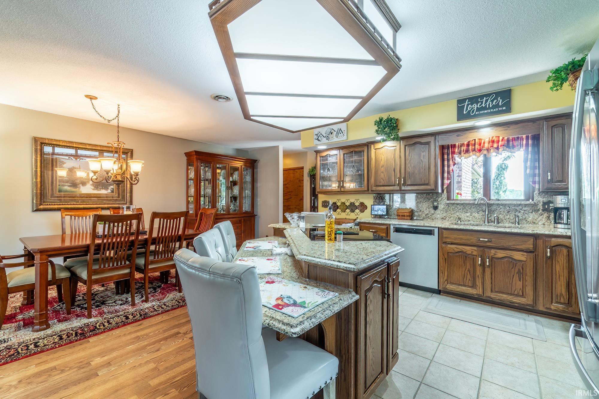 Kitchen and dining area featuring a central kitchen island with granite countertops, wood cabinetry, stainless steel appliances, and tile flooring
