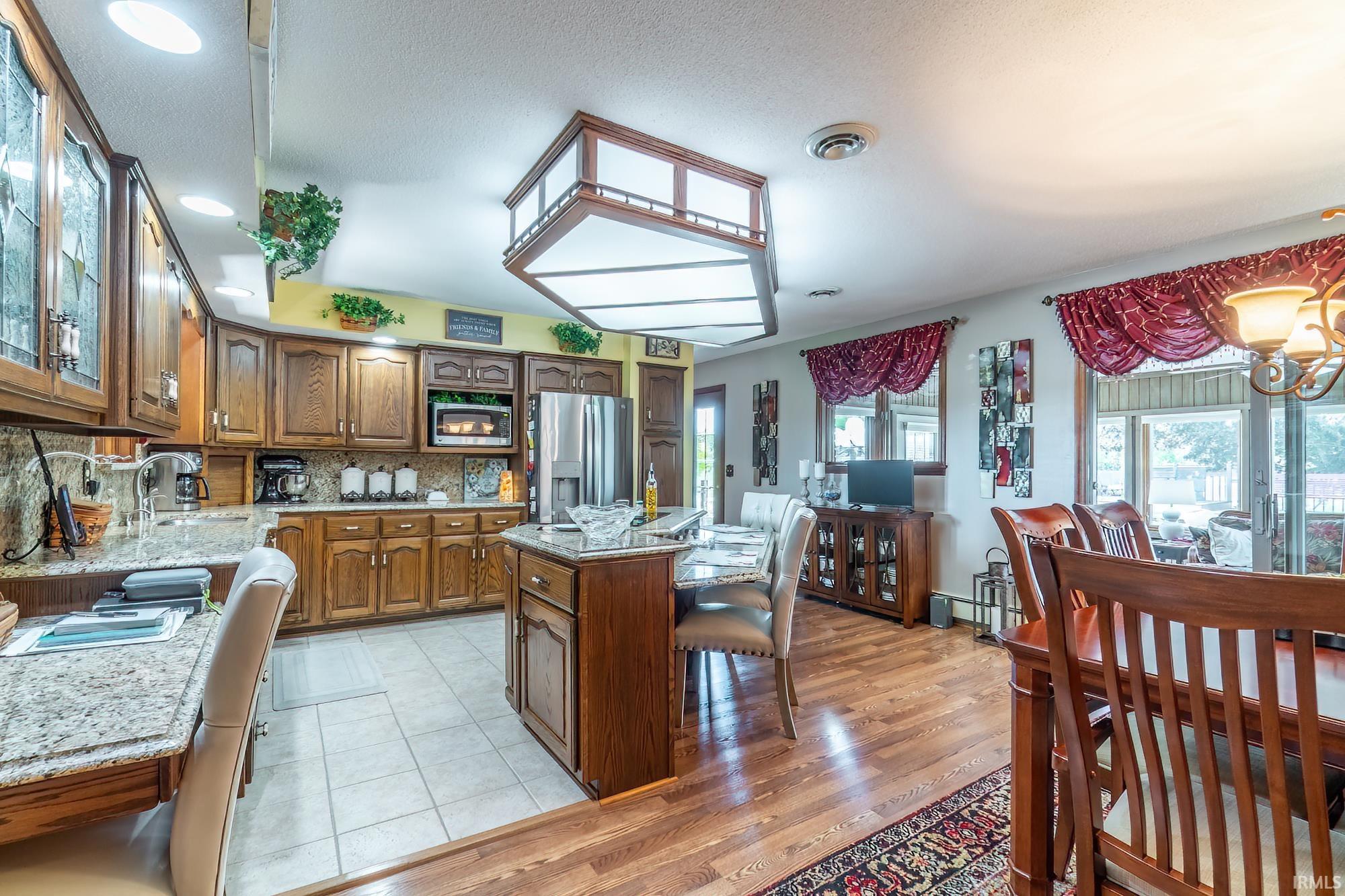 Open-concept kitchen and dining area featuring wood-finish cabinetry, light granite countertops, a built-in microwave, and stainless steel appliances
