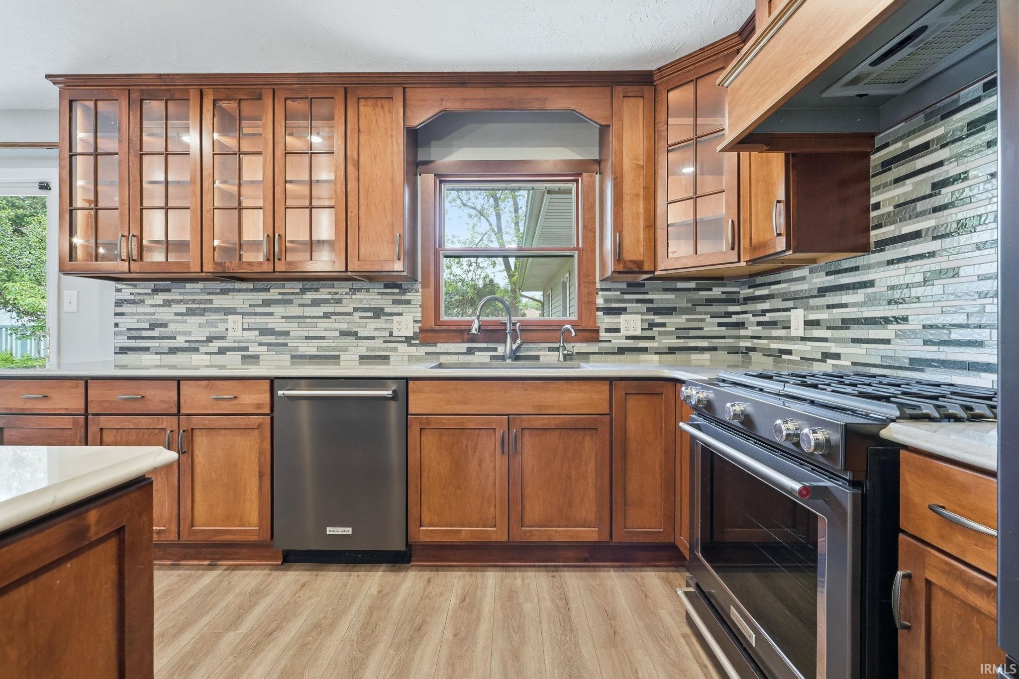 Kitchen featuring rich wood cabinetry, a mosaic tile backsplash, stainless steel appliances, and wood-finish flooring