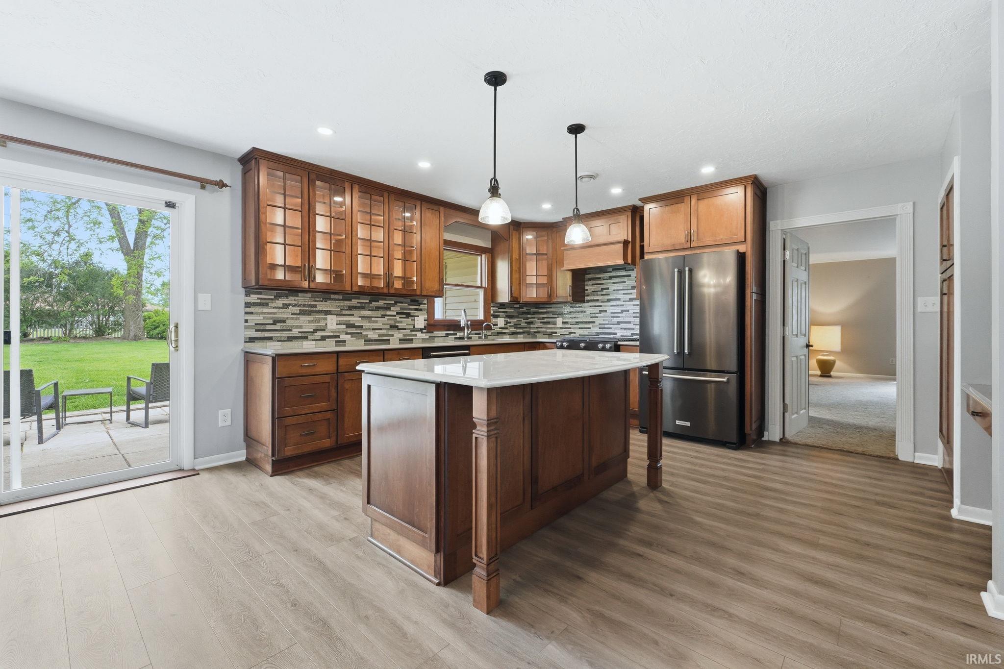 Kitchen featuring a central island with a light-colored countertop, wood-finish cabinetry, stainless steel refrigerator, and a mosaic tile backsplash