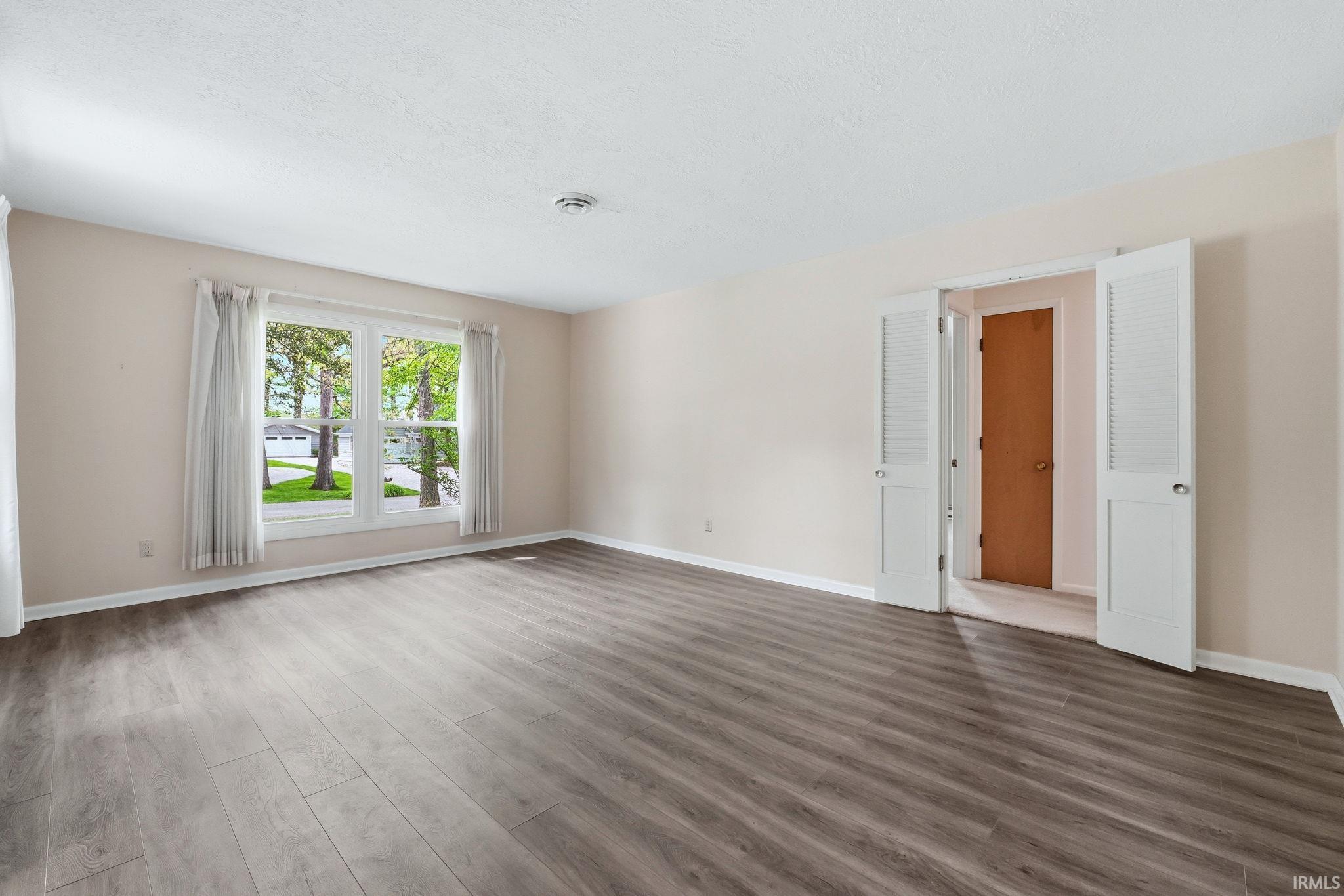 Spacious room with wood-finish flooring, light neutral wall paint, and a large window