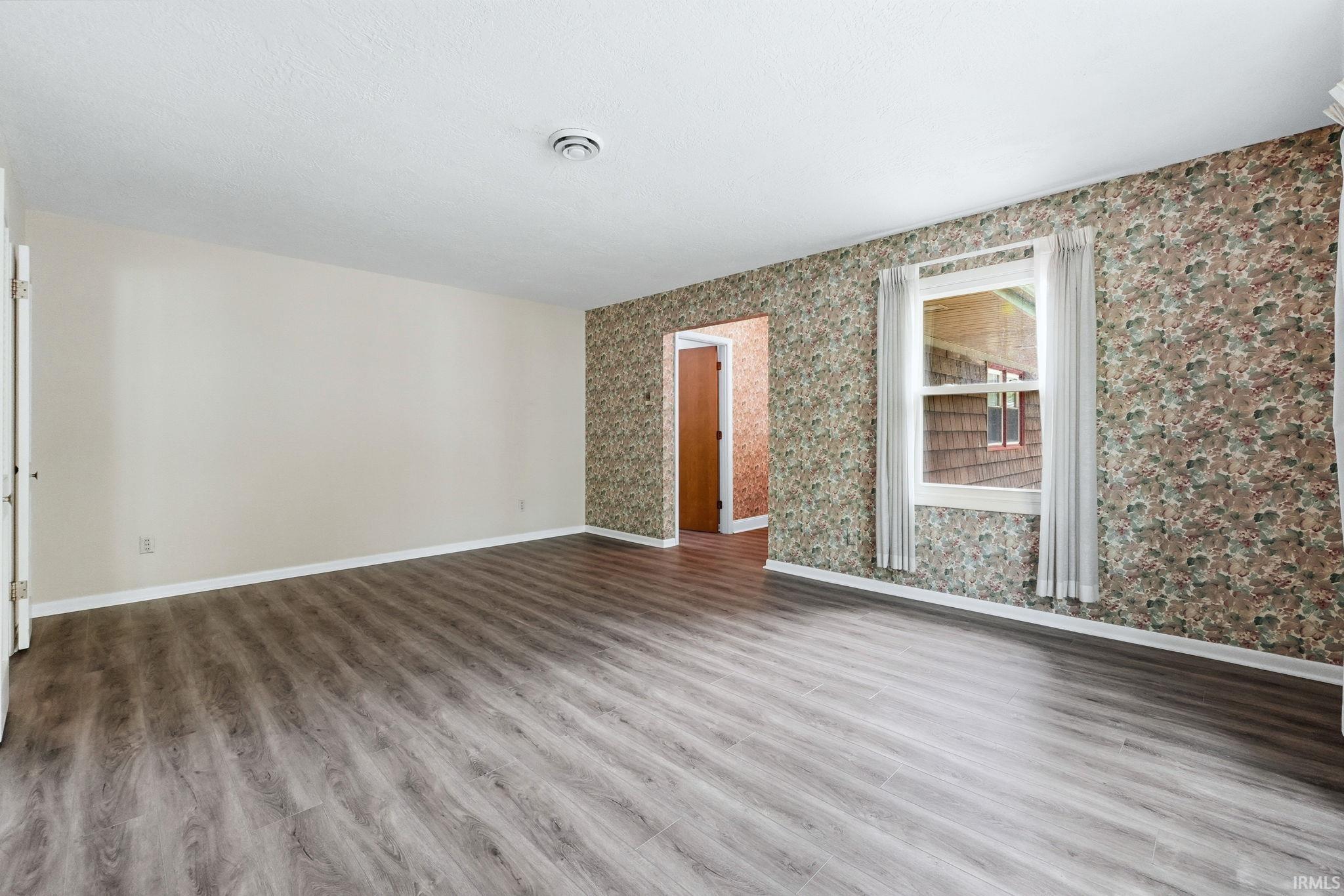 Spacious room featuring wood-finish flooring, a neutral wall, and a patterned accent wall