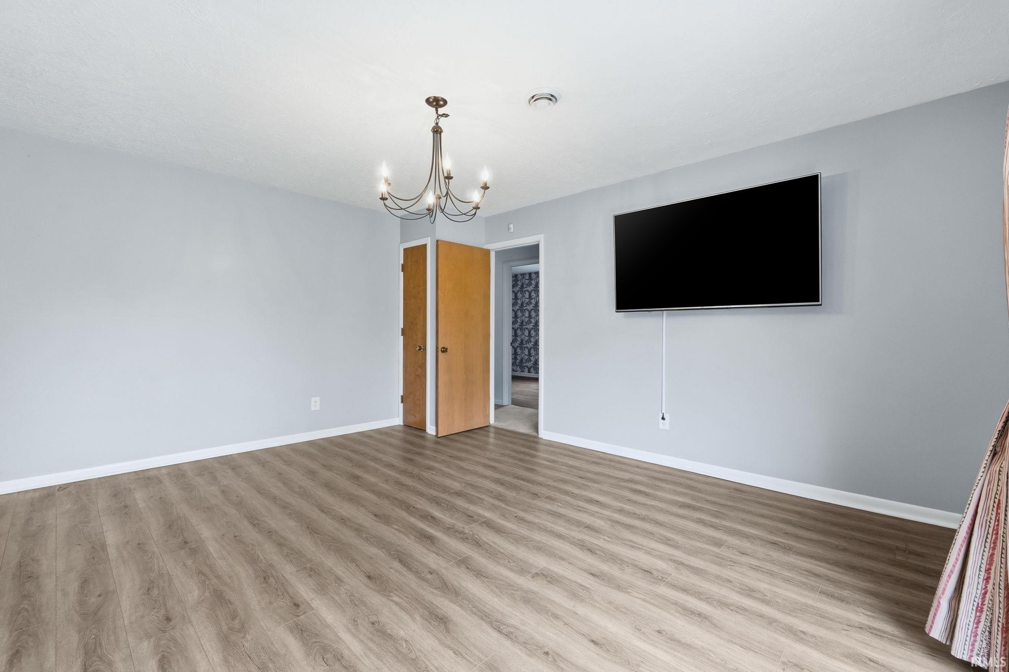 Spacious room featuring wood-finish flooring, light gray walls, white baseboards, and a chandelier with dark bronze-tone finish