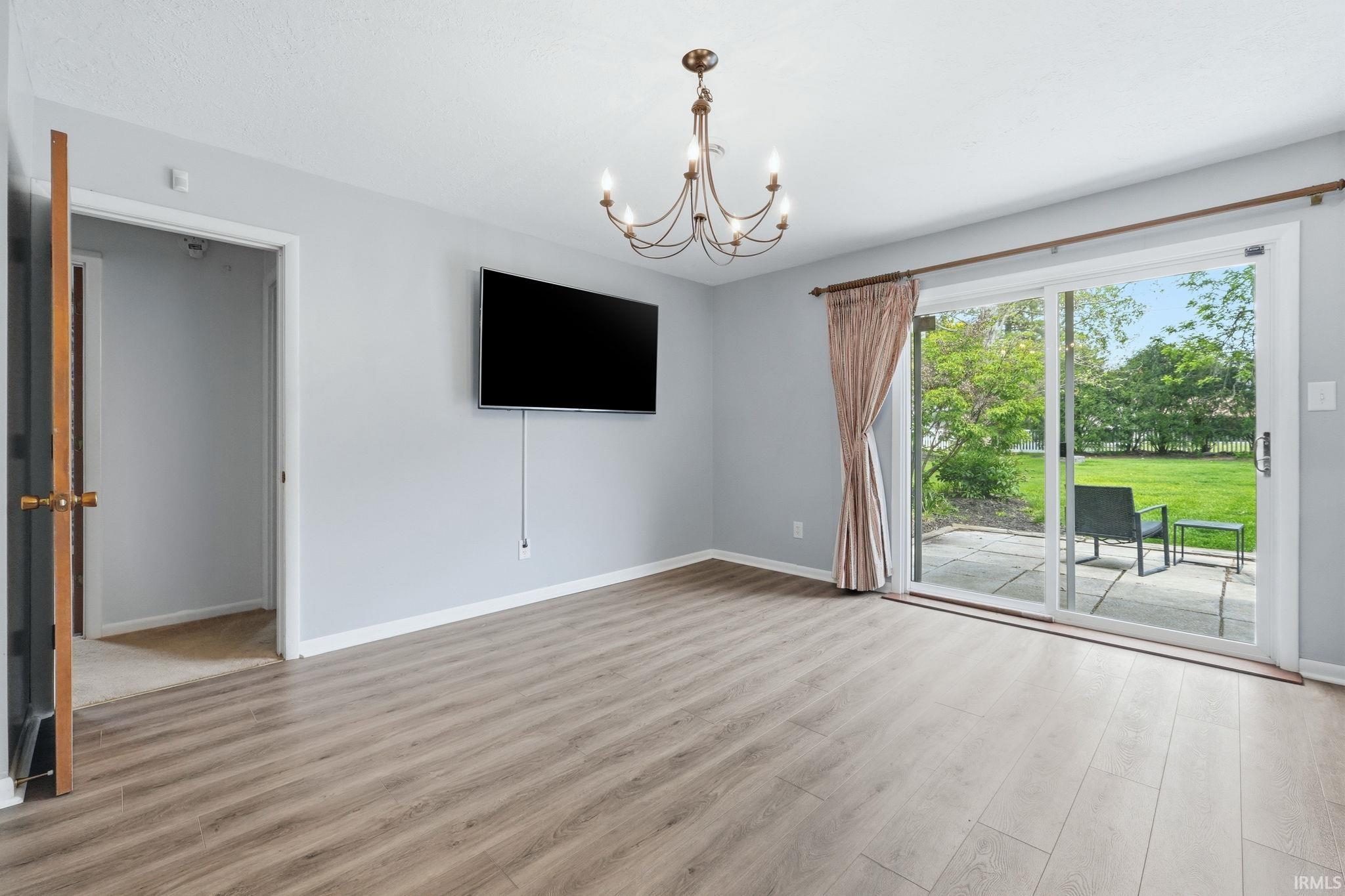 Spacious room featuring wood-finish flooring, a contemporary chandelier, and light gray wall tones