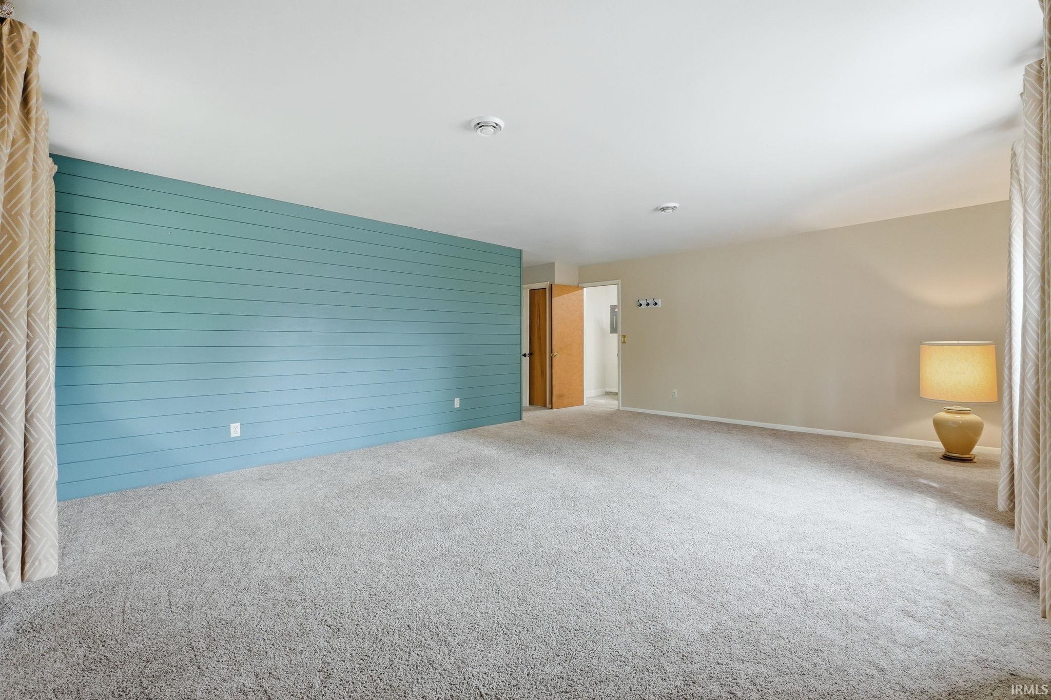 Spacious room featuring light gray carpeting and a prominent accent wall with horizontal paneling