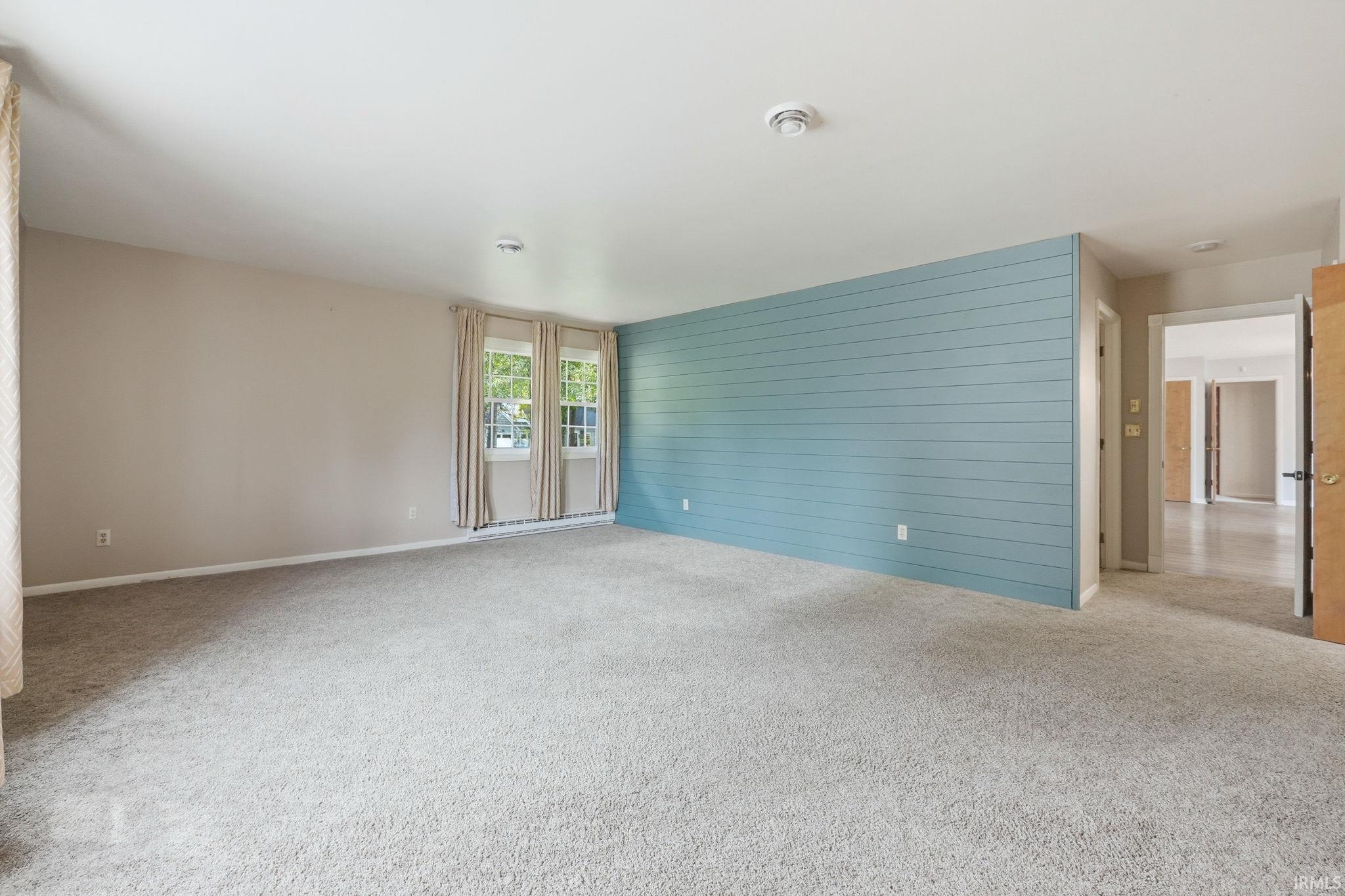 Spacious room featuring light-colored carpeting, multiple windows, a blue shiplap accent wall, and neutral wall tones