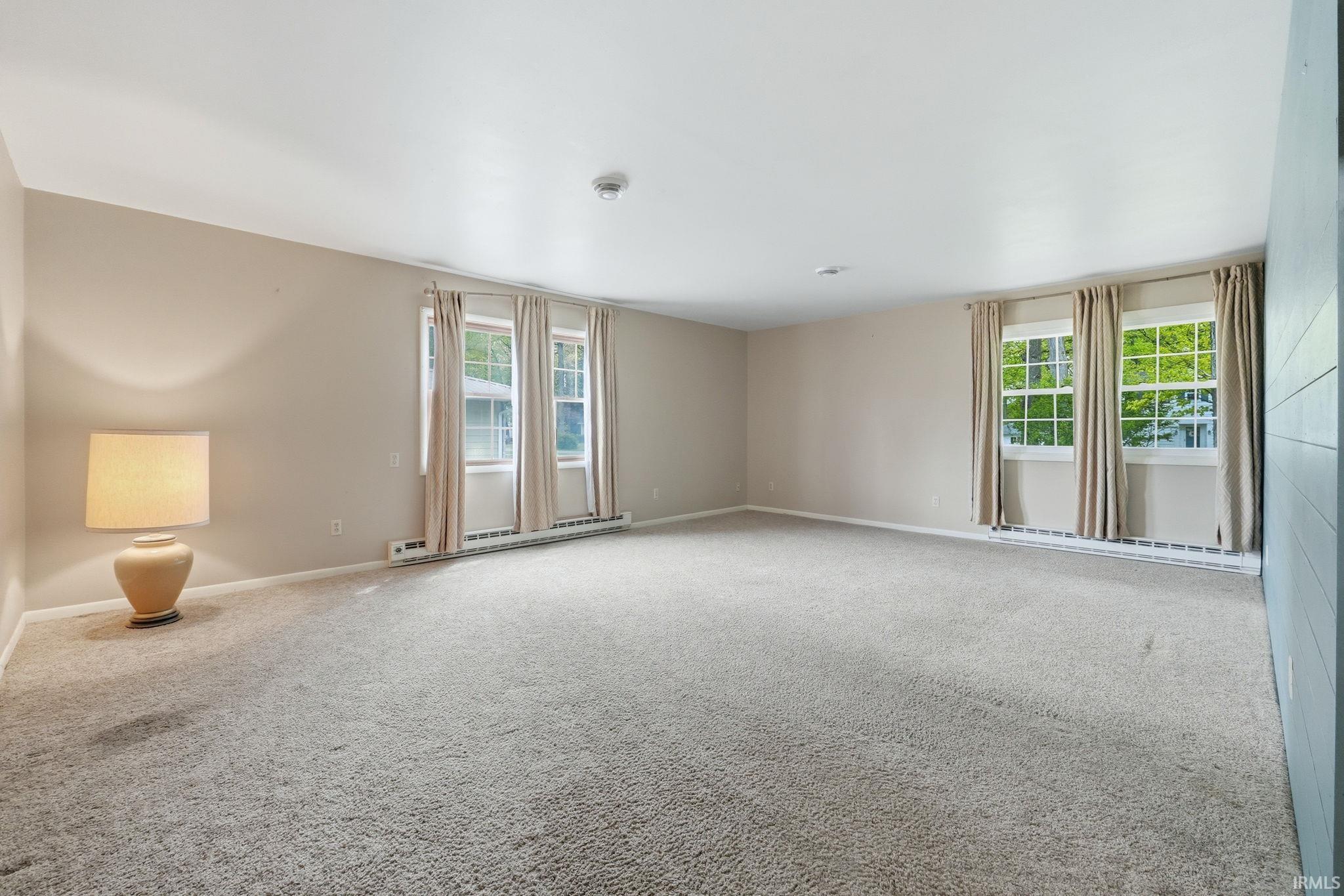 Spacious room featuring neutral carpeting, multiple windows with curtains, and light-toned wall finishes