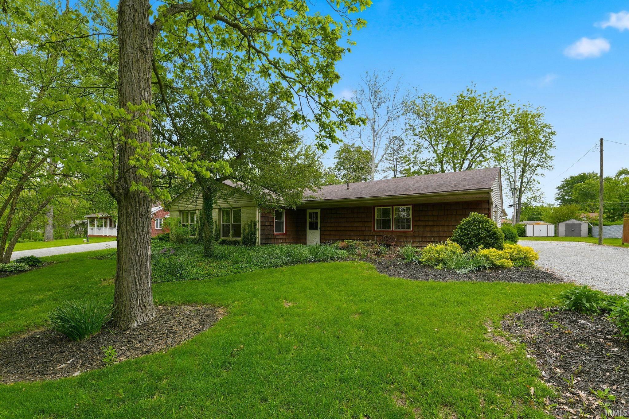 Ranch-style exterior with shingle siding, a gravel driveway, and mature landscaping