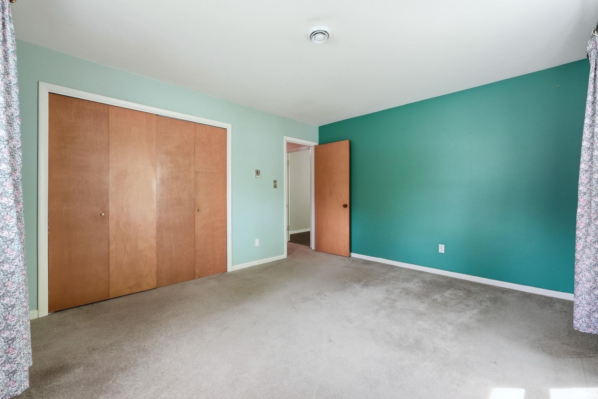 Carpeted interior space featuring a full-wall closet with four light wood-finish doors, a doorway with a light wood-finish door, and walls painted in contrasting shades of green and teal