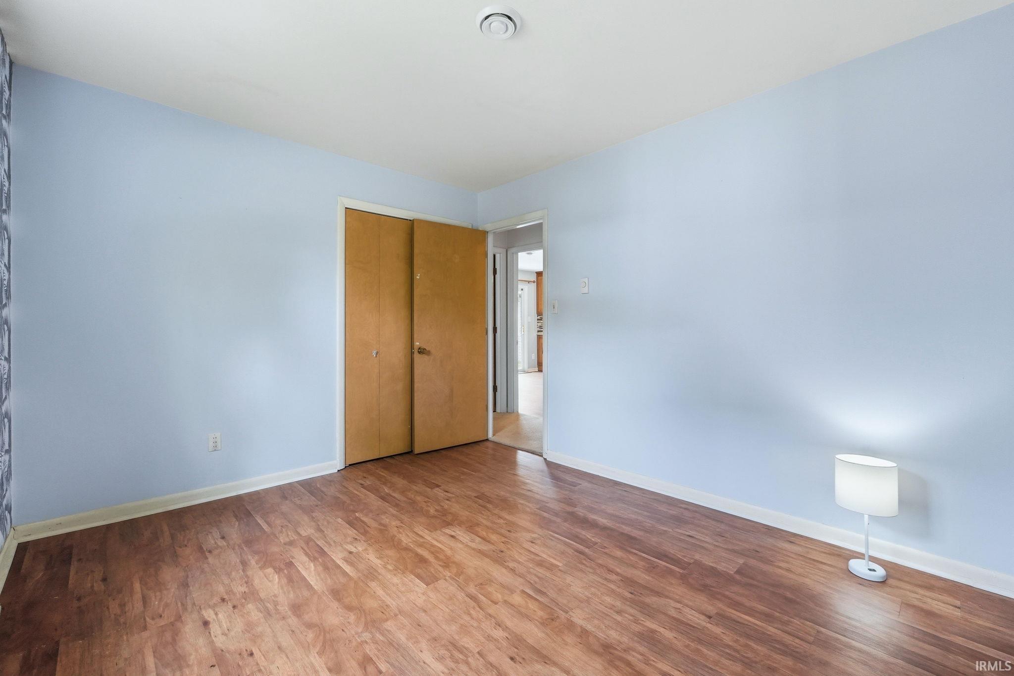 Spacious room featuring wood-finish flooring, light blue walls, white trim, and a ceiling light fixture