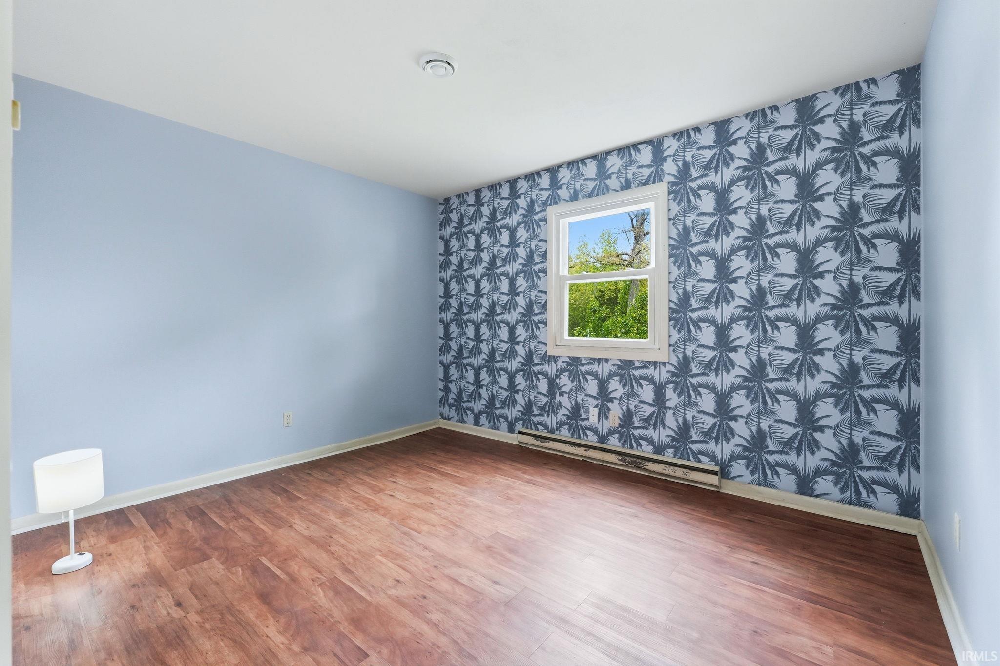 Room featuring wood-finish flooring, a wall with palm frond pattern wallpaper, and light blue painted walls