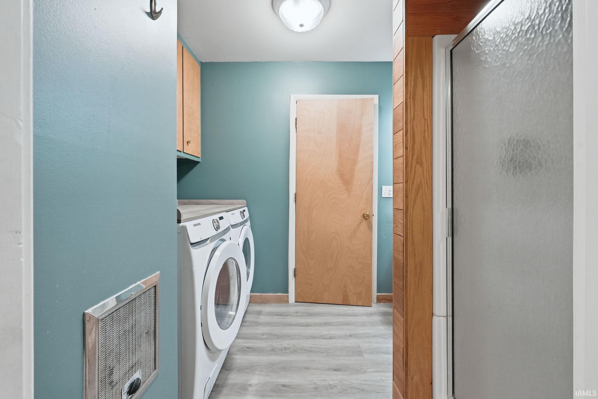 Laundry area featuring wood-finish flooring, light wood cabinetry, and a countertop surface