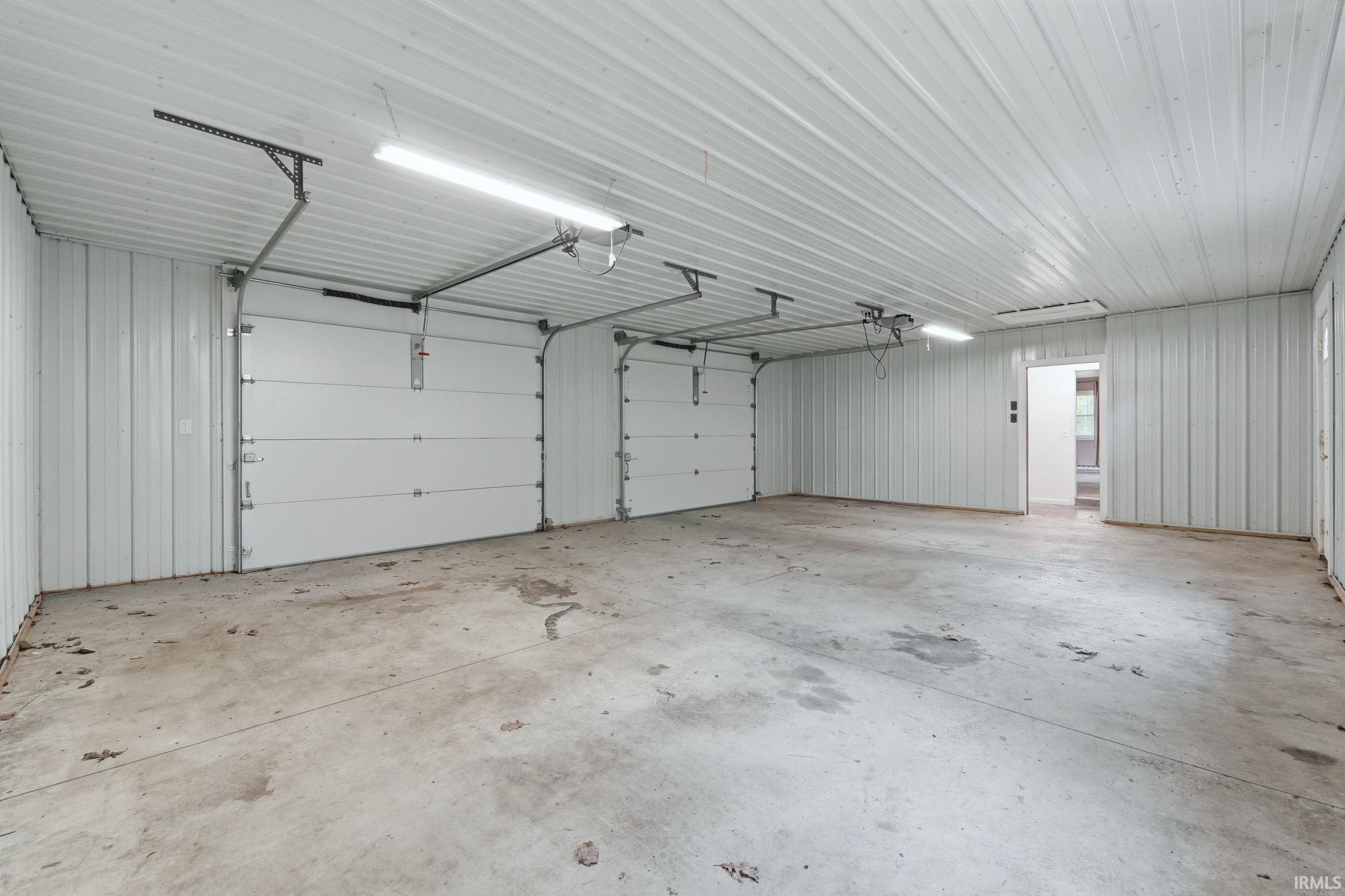 Spacious garage featuring two overhead doors with automatic openers, corrugated metal walls and ceiling, concrete flooring, and fluorescent lighting