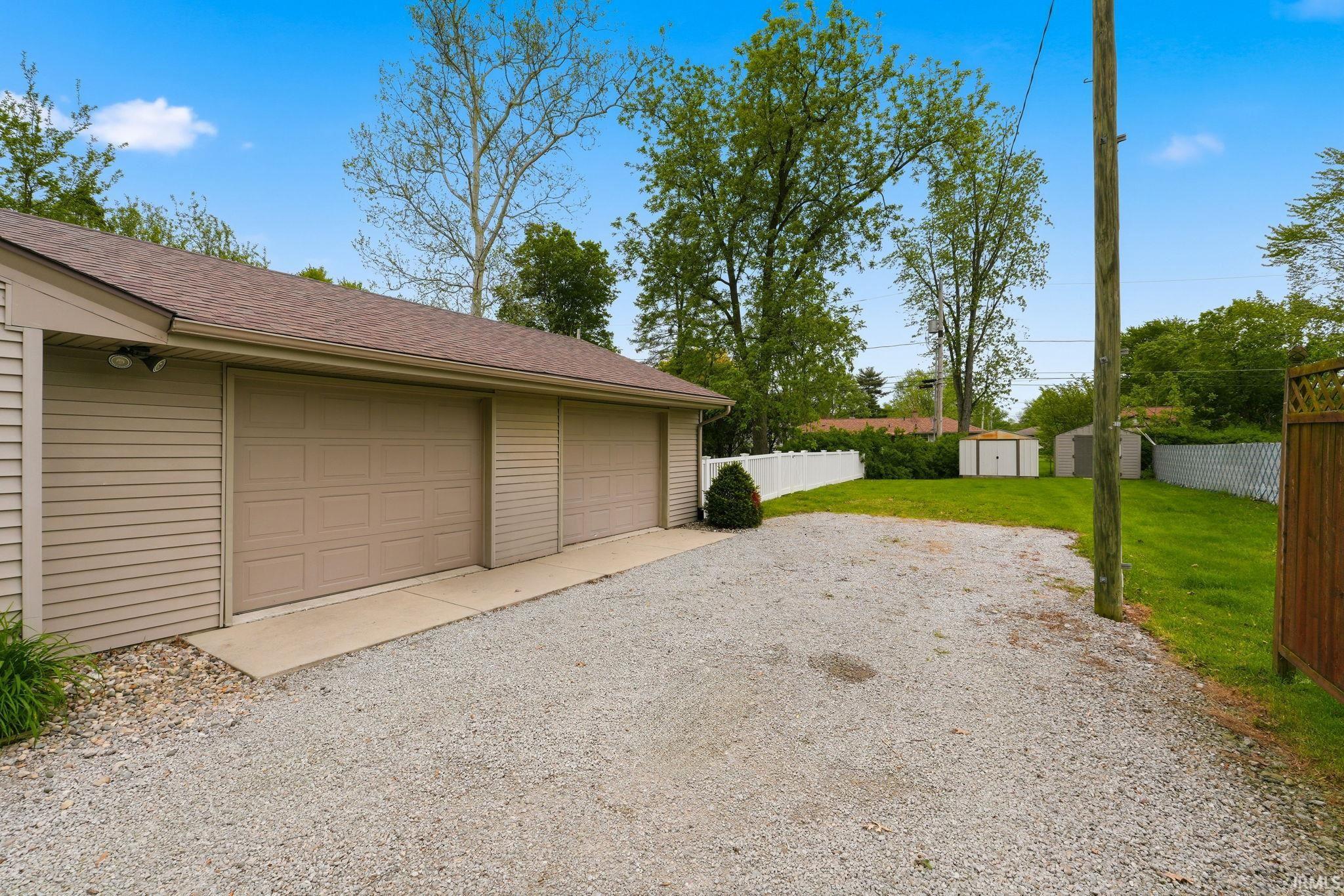 Two-car garage with tan siding, brown paneled garage doors, and a gravel driveway