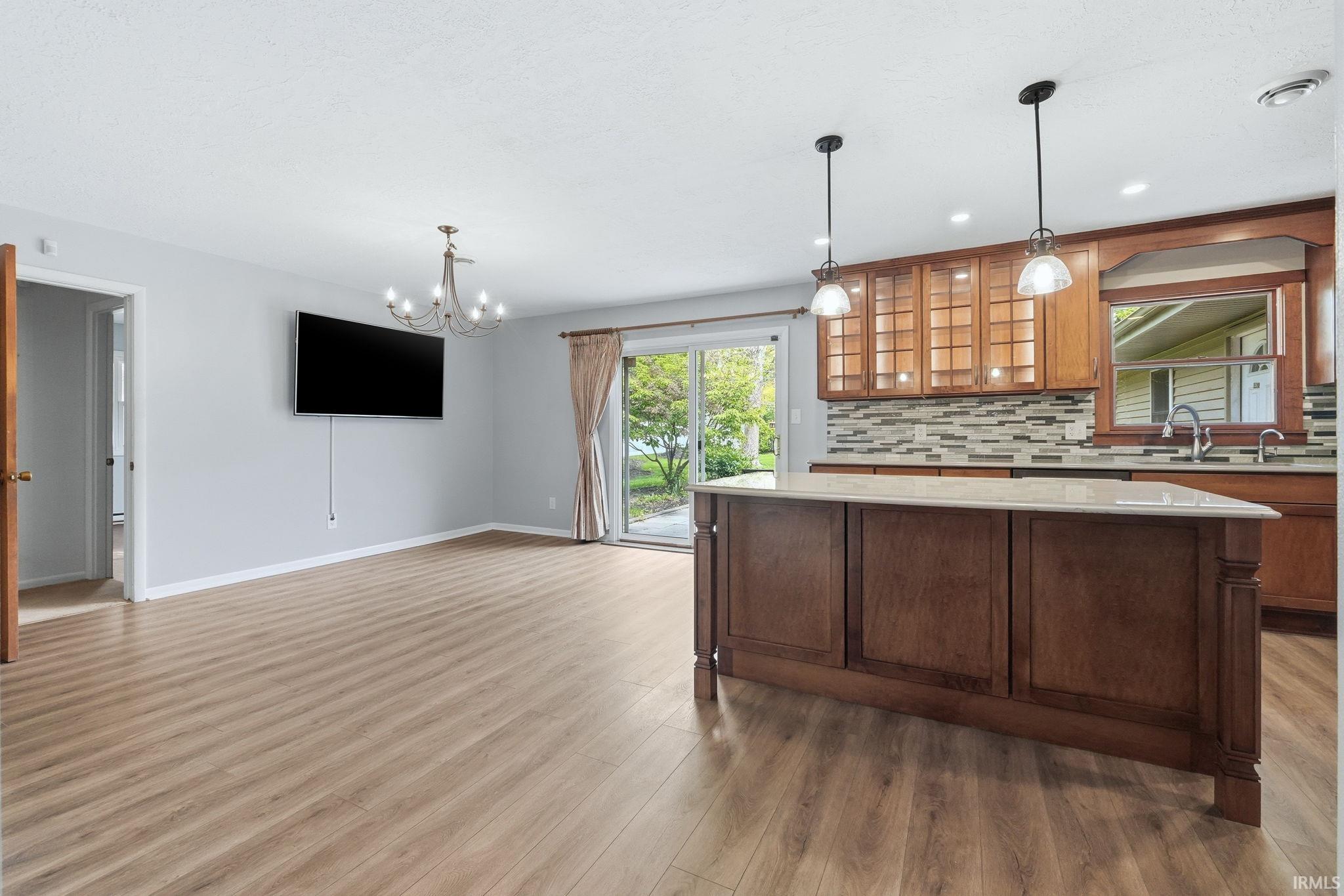 Open-concept living space featuring wood-finish flooring, a kitchen island with a light-toned countertop, and pendant lighting