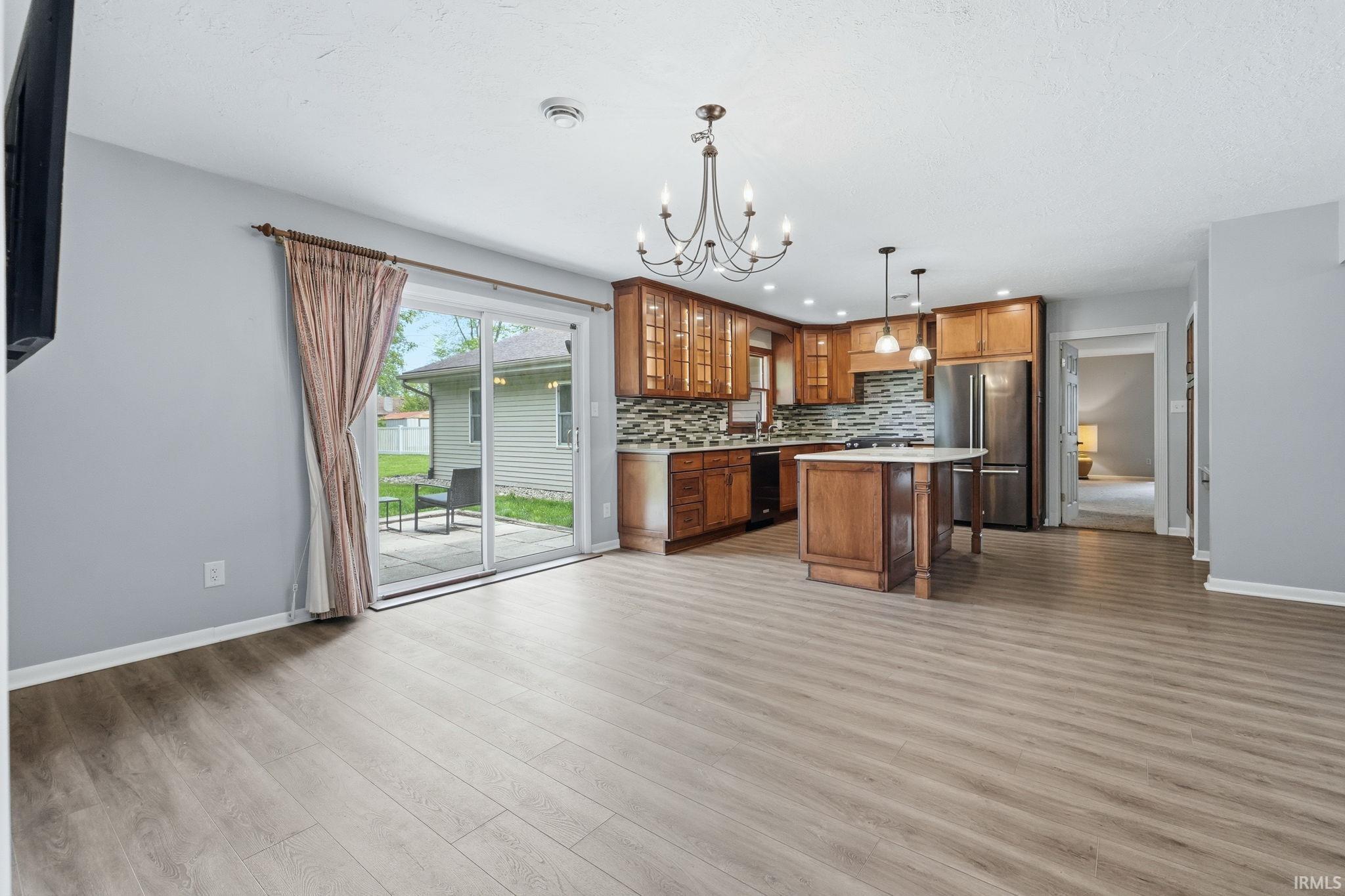 Open-concept living space featuring wood-finish flooring, a kitchen island with seating, stainless steel appliances, a tiled backsplash, and a sliding glass door leading to an outdoor patio area