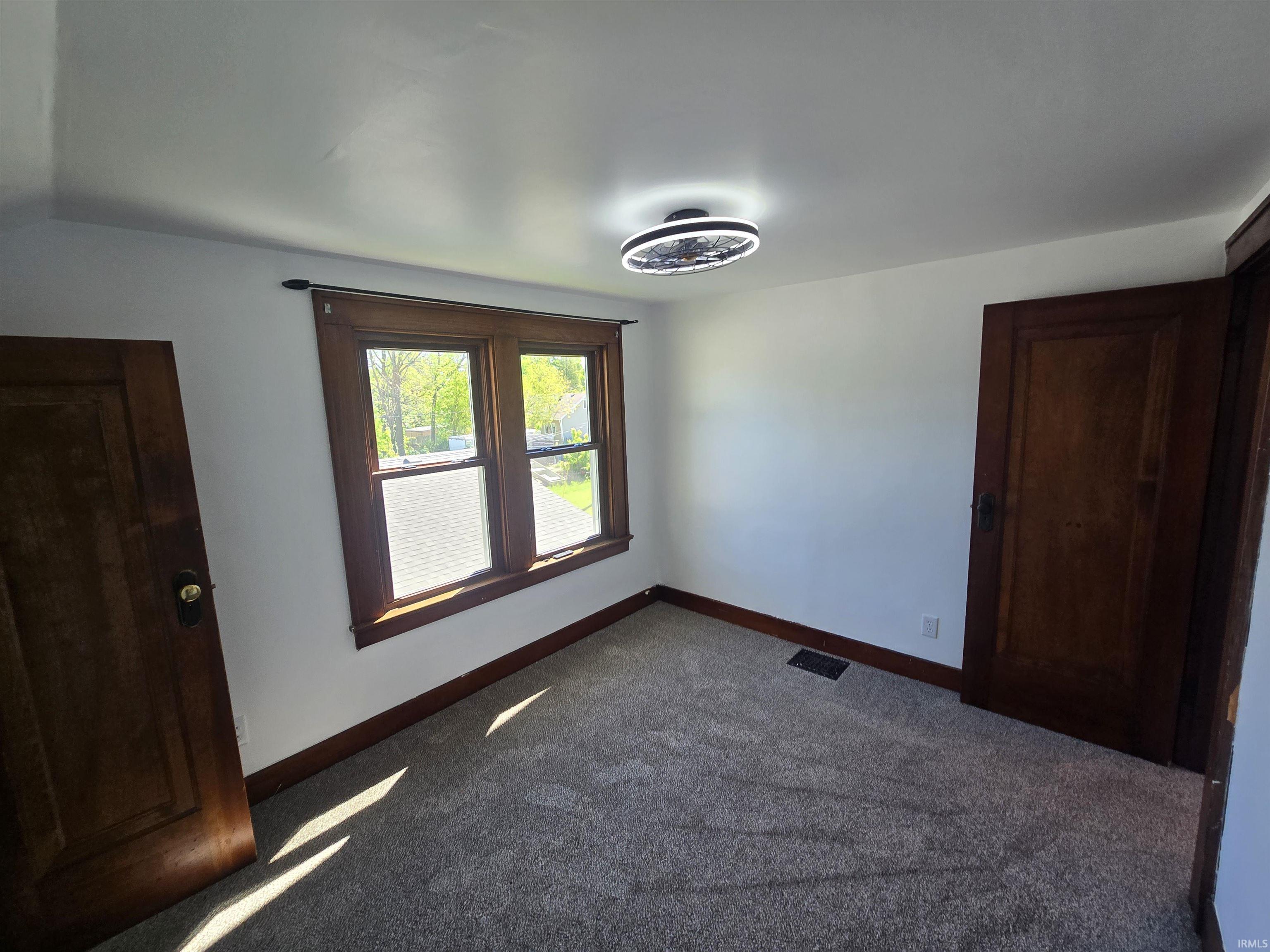 Interior room featuring a double window with wood trim, wood-paneled doors, a modern flush-mount ceiling light fixture, and textured carpeting