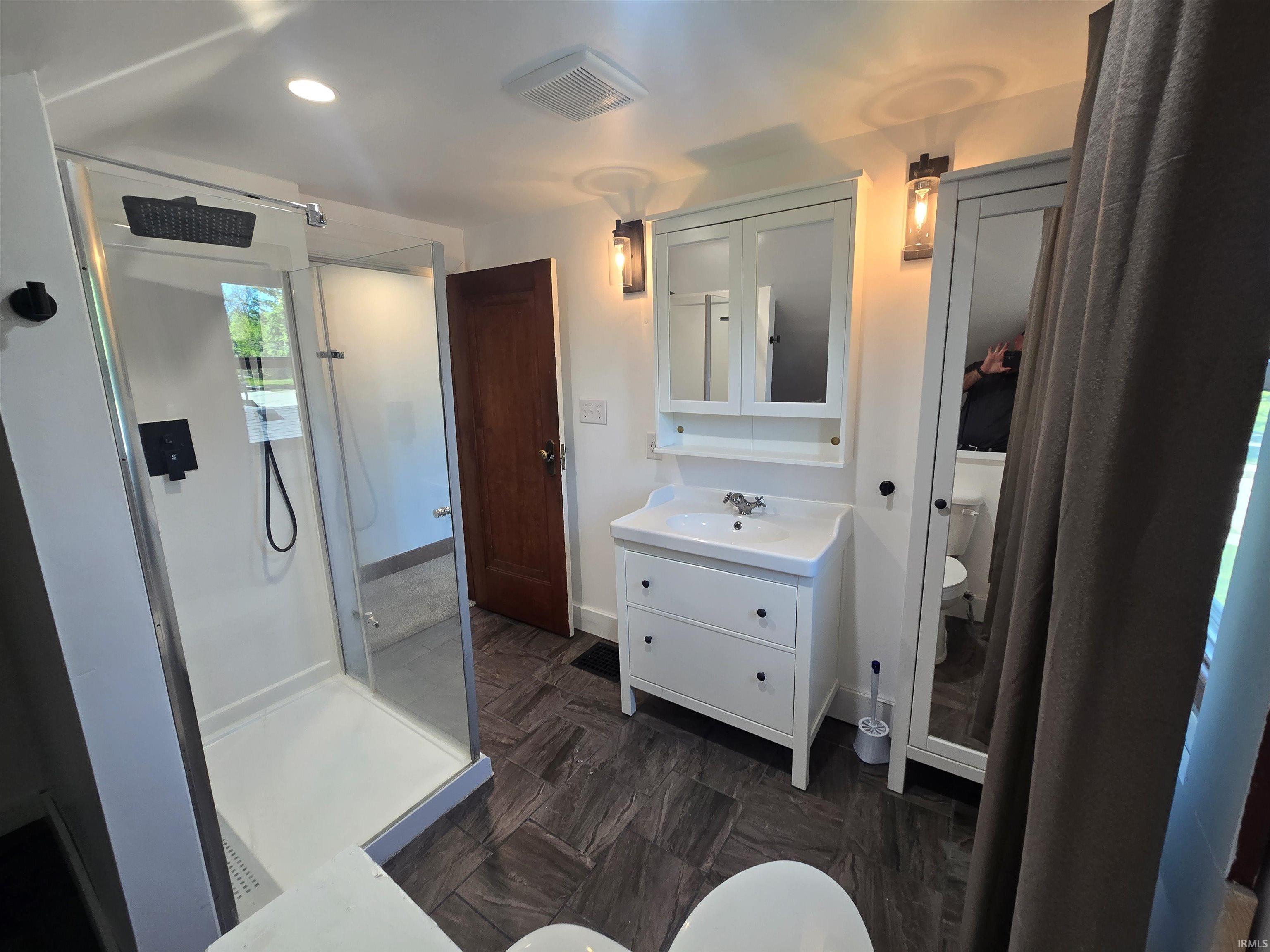 Bathroom featuring a glass-enclosed shower with black fixtures, a single-sink vanity with white cabinetry, a mirrored medicine cabinet, and wall-mounted sconces