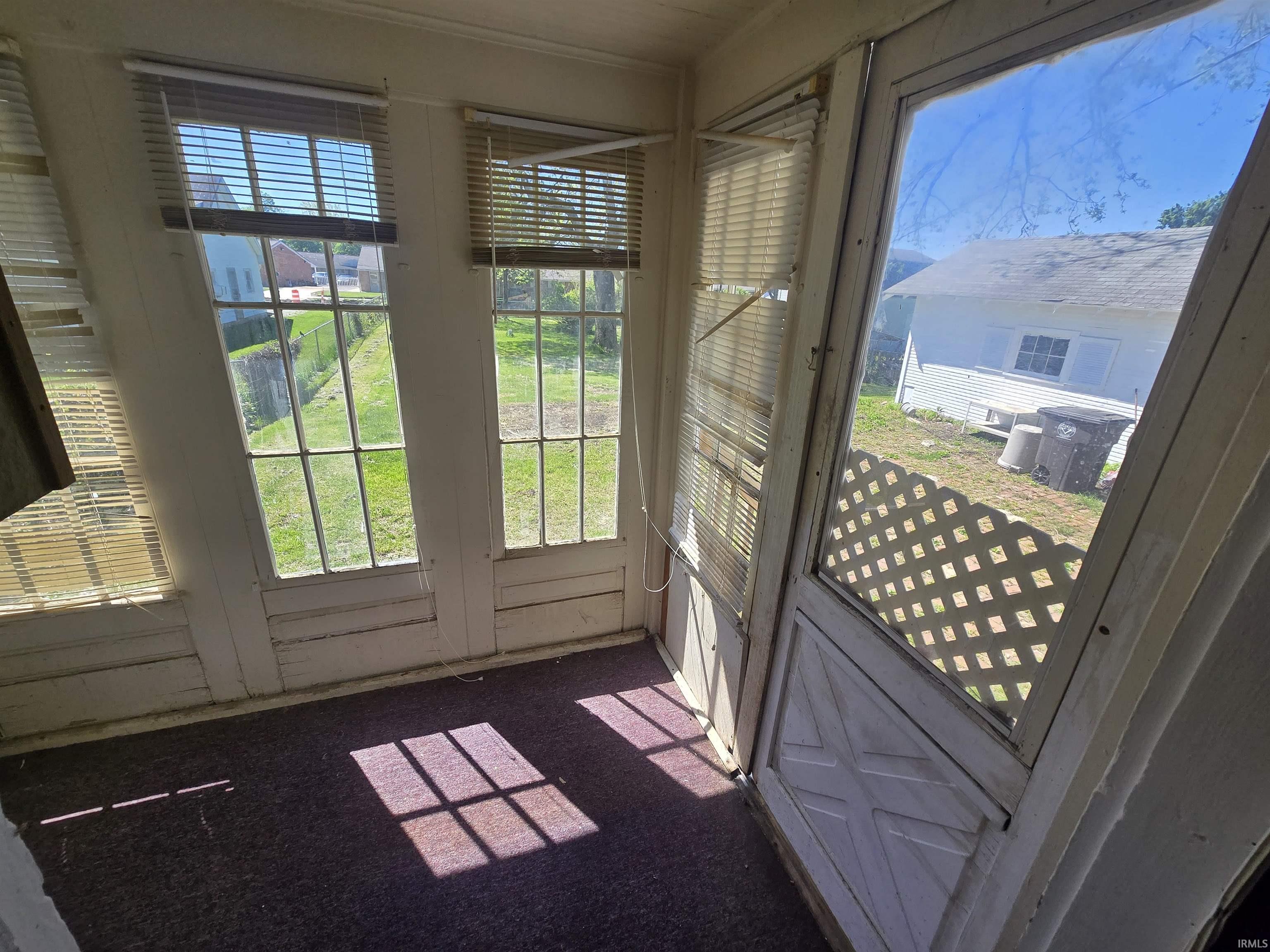 Enclosed porch featuring multiple windows with blinds, a screen door with a lattice accent, and carpeted flooring