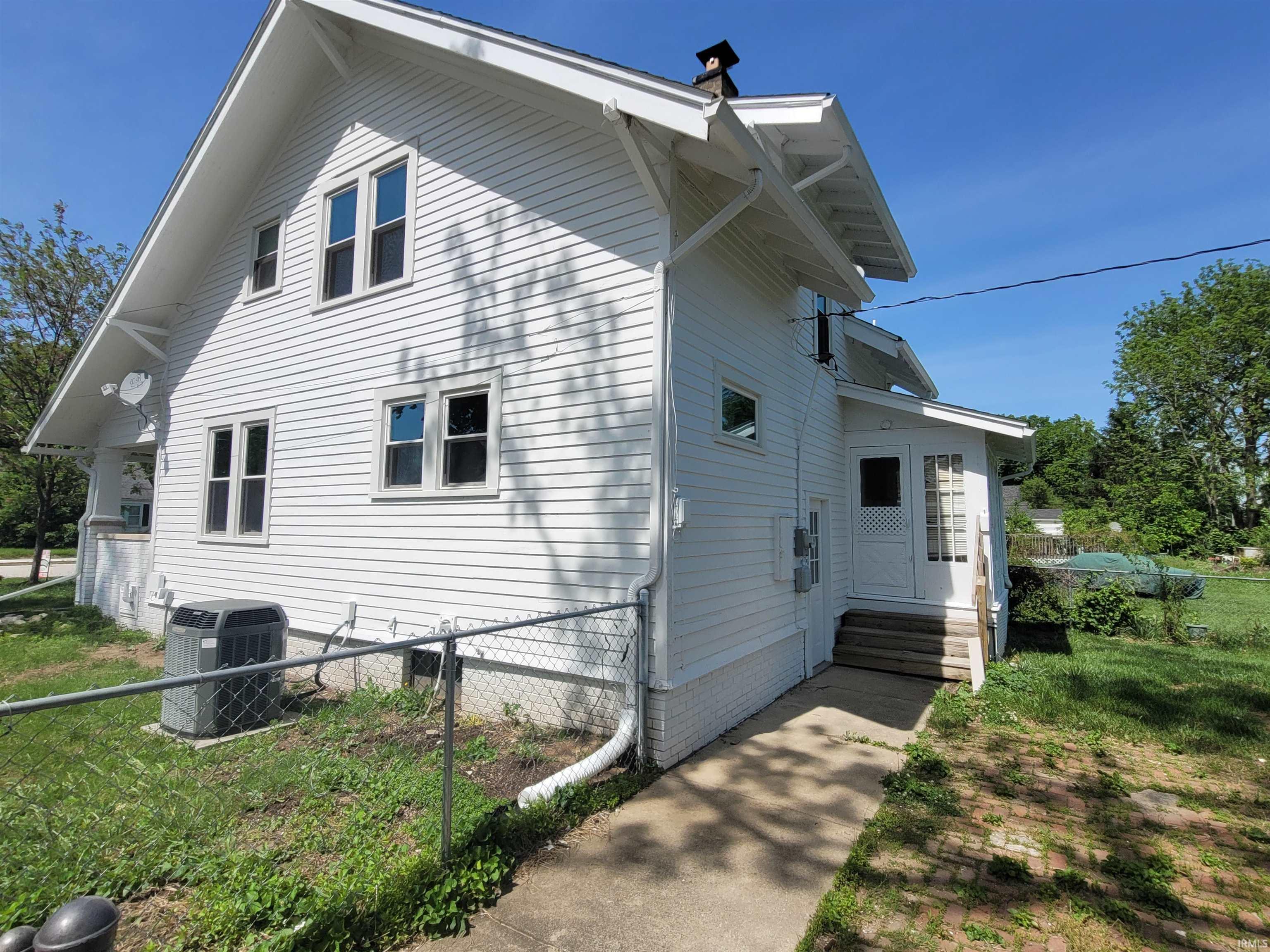 White siding exterior with multiple windows, a gabled roofline, and an enclosed porch entry