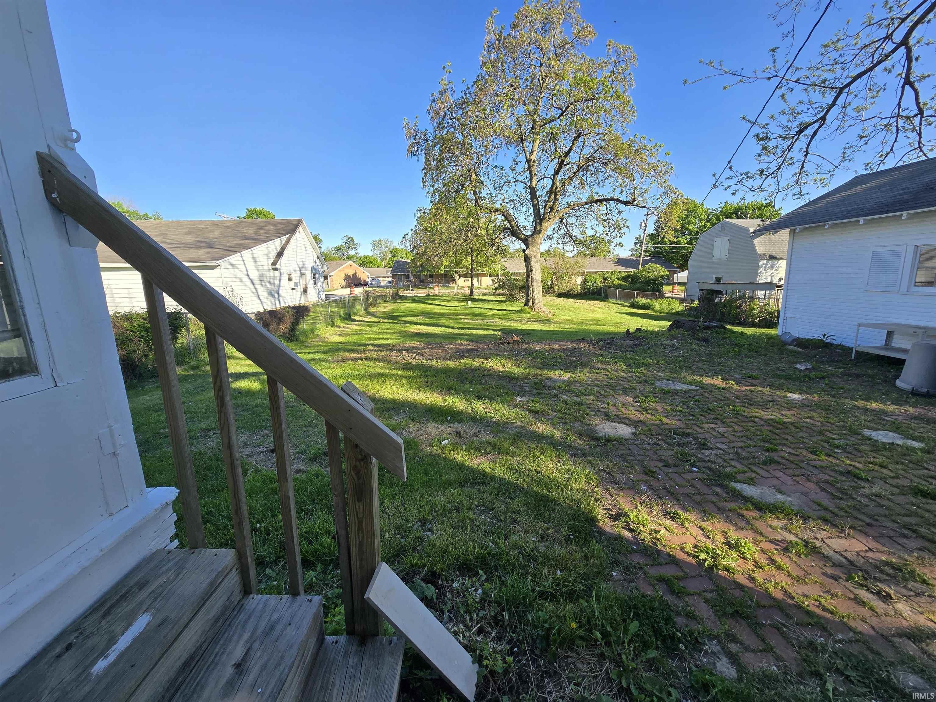 Expansive outdoor space featuring a large grassy area, mature tree, and a brick paver patio