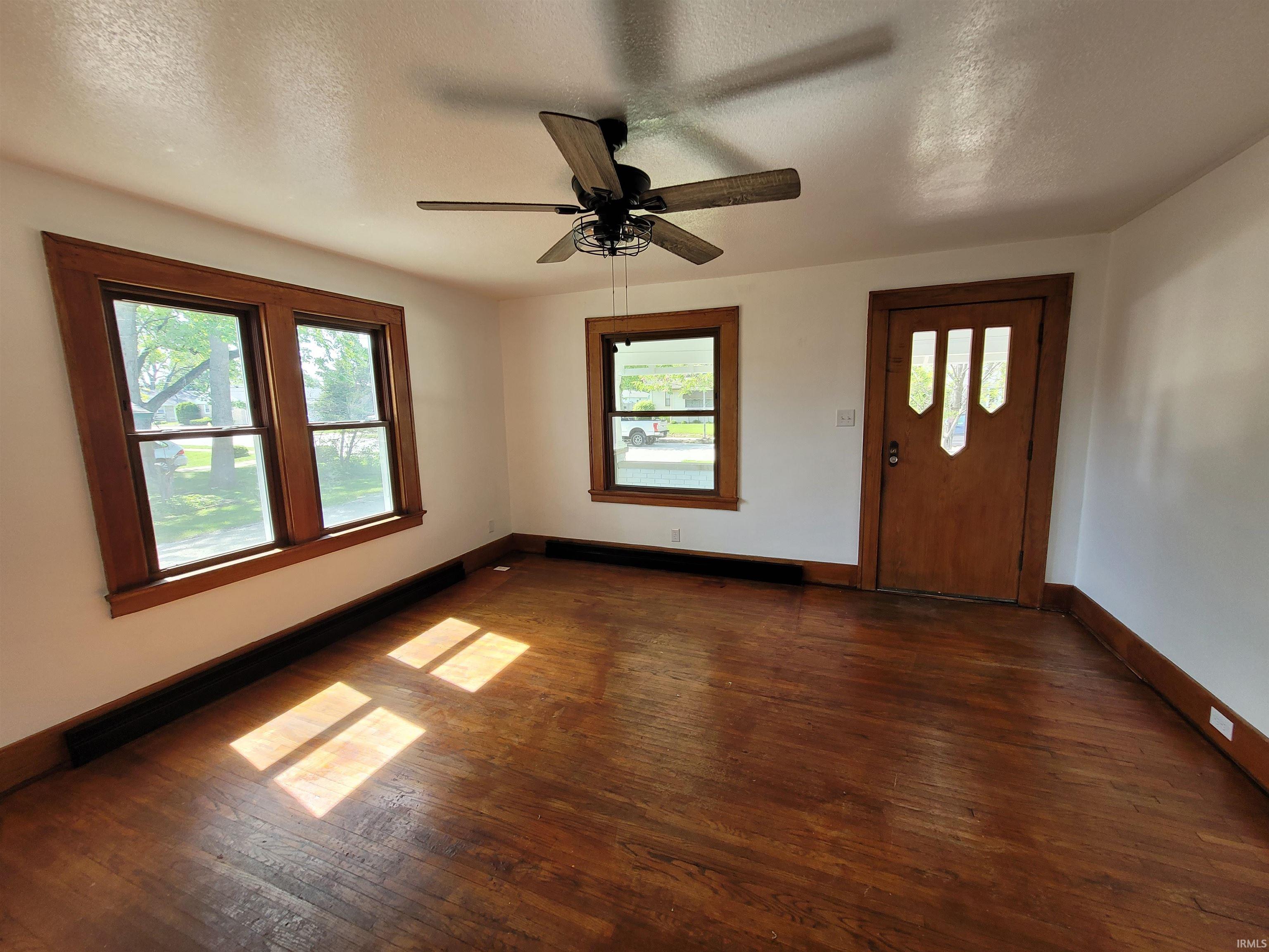 Spacious room featuring wood-finish flooring, white walls, and prominent wood trim around windows and doors